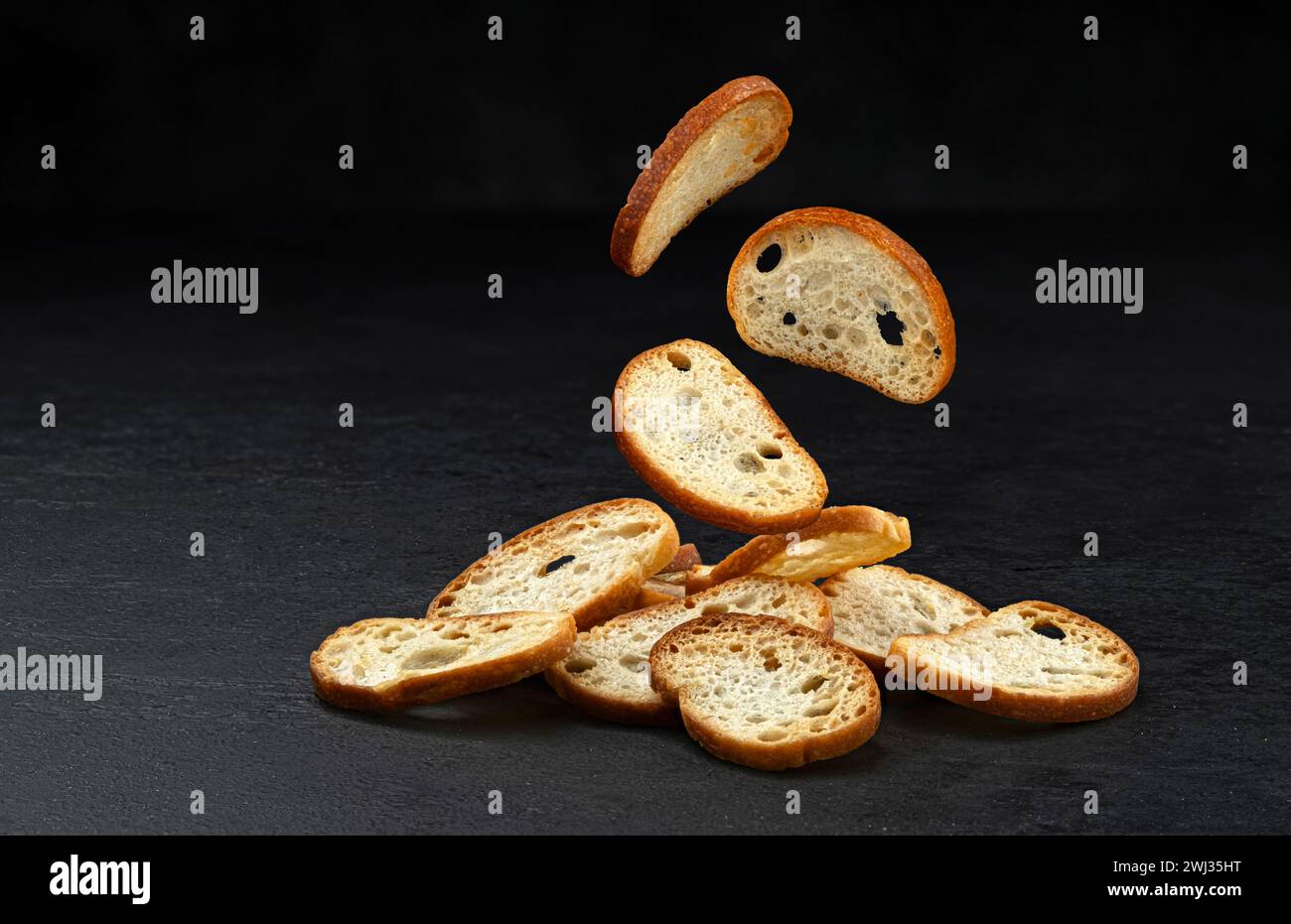 Fallende Bruschetta-Cracker, runde Brotcroutons isoliert auf schwarzem Hintergrund Stockfoto