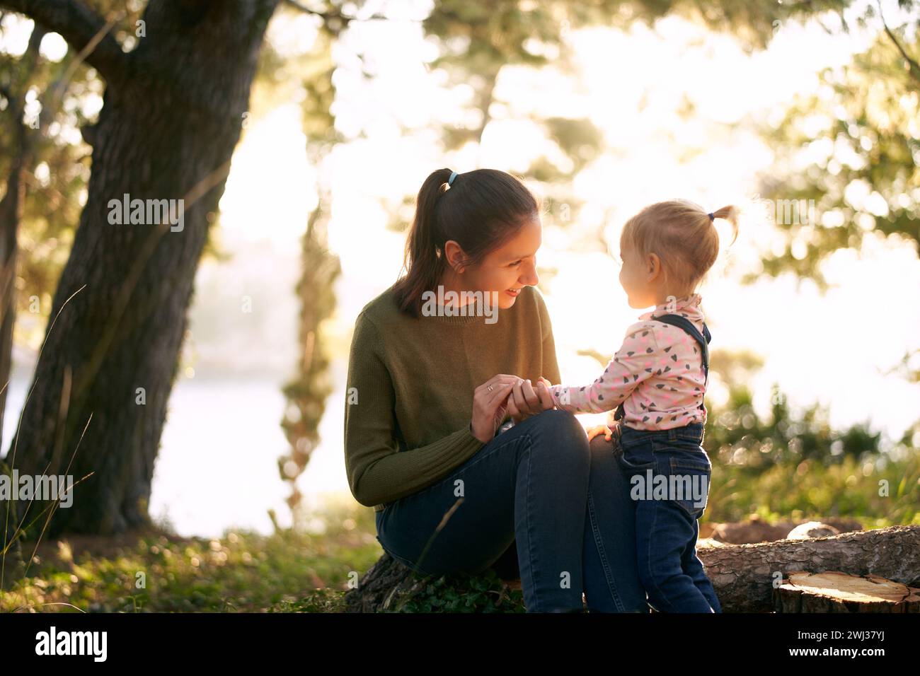 Die lächelnde Mutter lehrt einem kleinen Mädchen, sich darauf zu verlassen, dass ihre Finger auf einem Baumstumpf im Wald sitzen Stockfoto