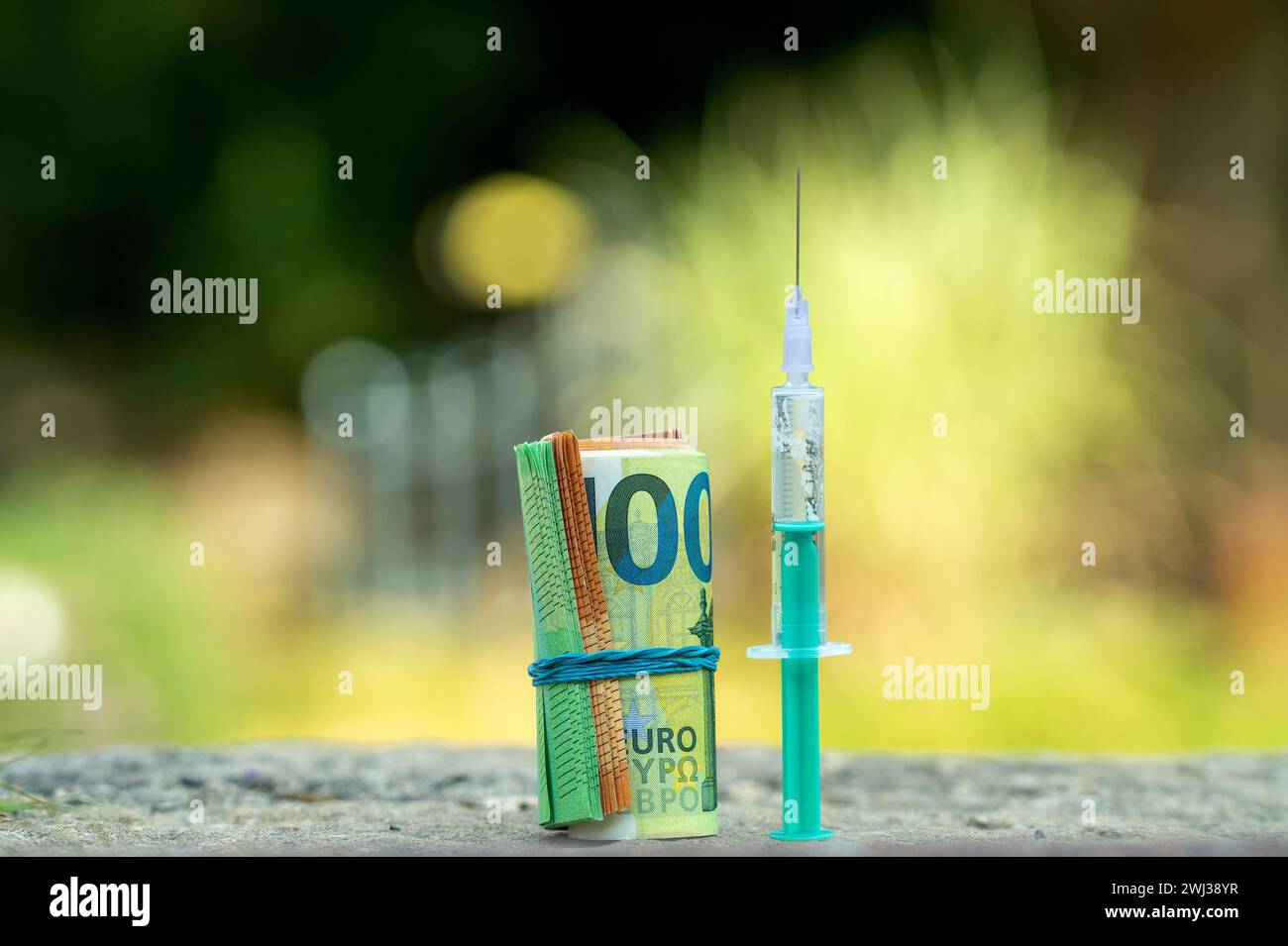 Spritze und Euro-Geldrolle. 100- und 50-Euro-Scheine, die in einen Schlauch gewickelt und mit einem Gummiband gebunden sind. Stockfoto