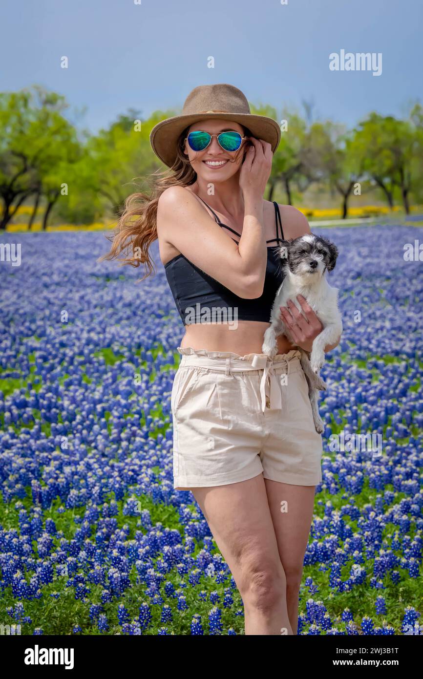 Ein schönes Brünette Model posiert in Einem Feld mit Bluebonnet-Blumen mit ihrem Hund in Einem Texas Prarie Stockfoto