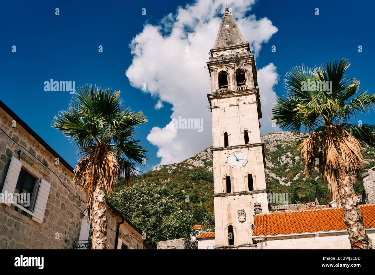 Glockenturm der Kirche St. Nikolaus mit einer Uhr zwischen alten Häusern vor dem Hintergrund grüner Berge. Perast, Mont Stockfoto