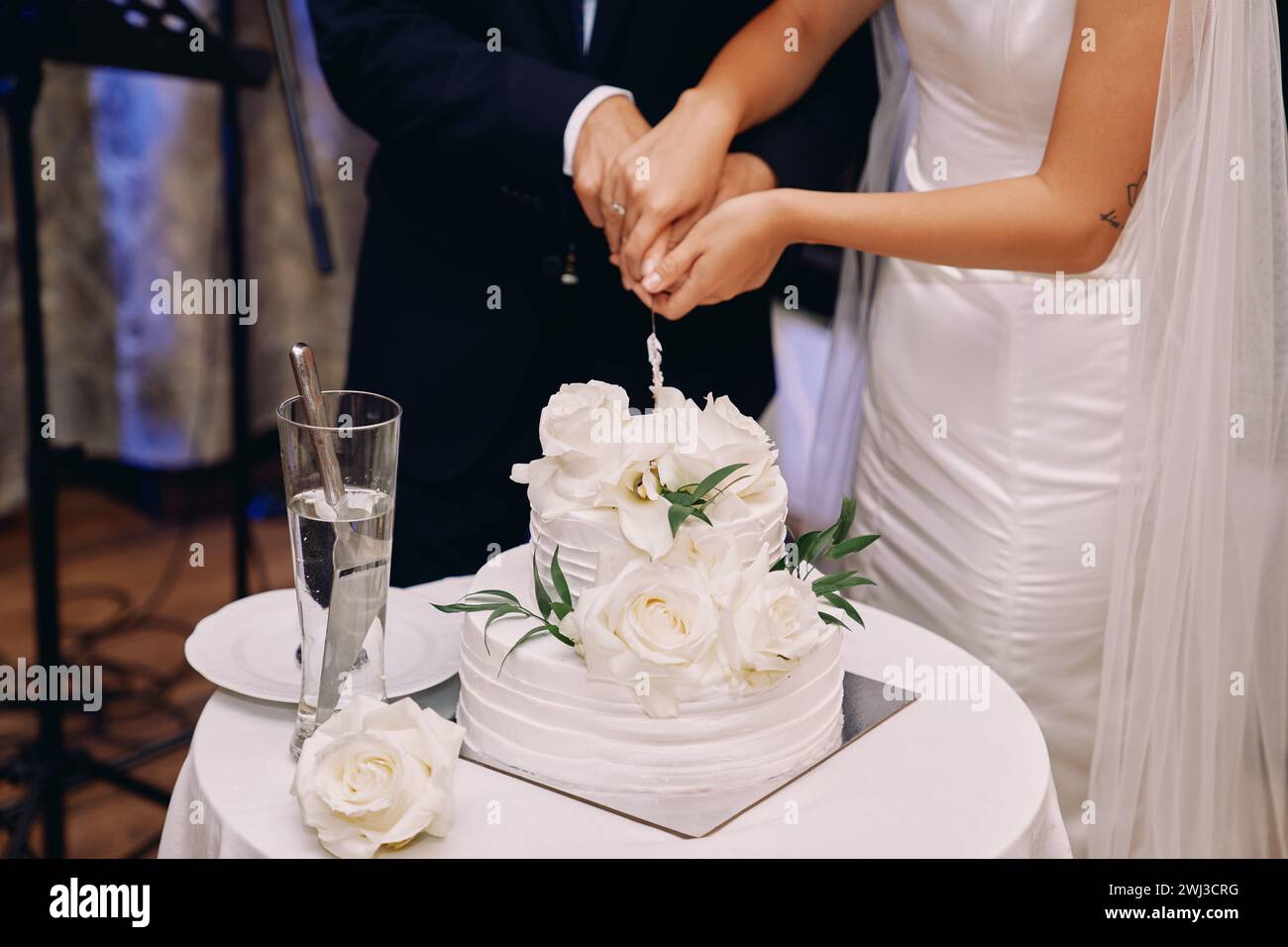 Braut und Bräutigam schnitten eine Hochzeitstorte mit einem Messer auf einem Tisch. Abgeschnitten. Gesichtslos Stockfoto