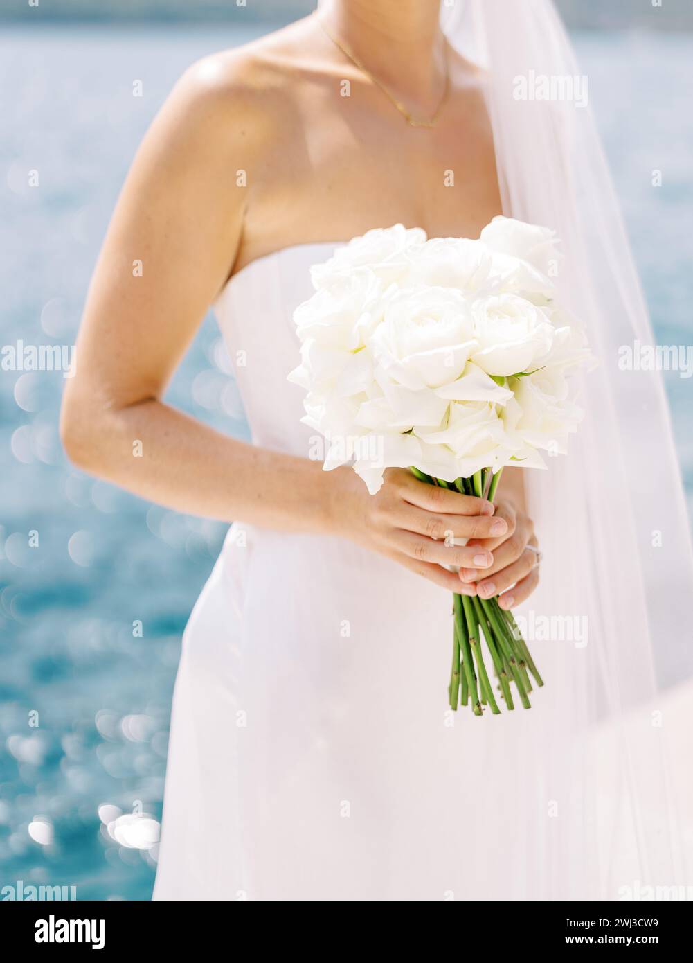 Blumenstrauß in den Händen einer Braut, die am Meer steht. Abgeschnitten. Gesichtslos Stockfoto