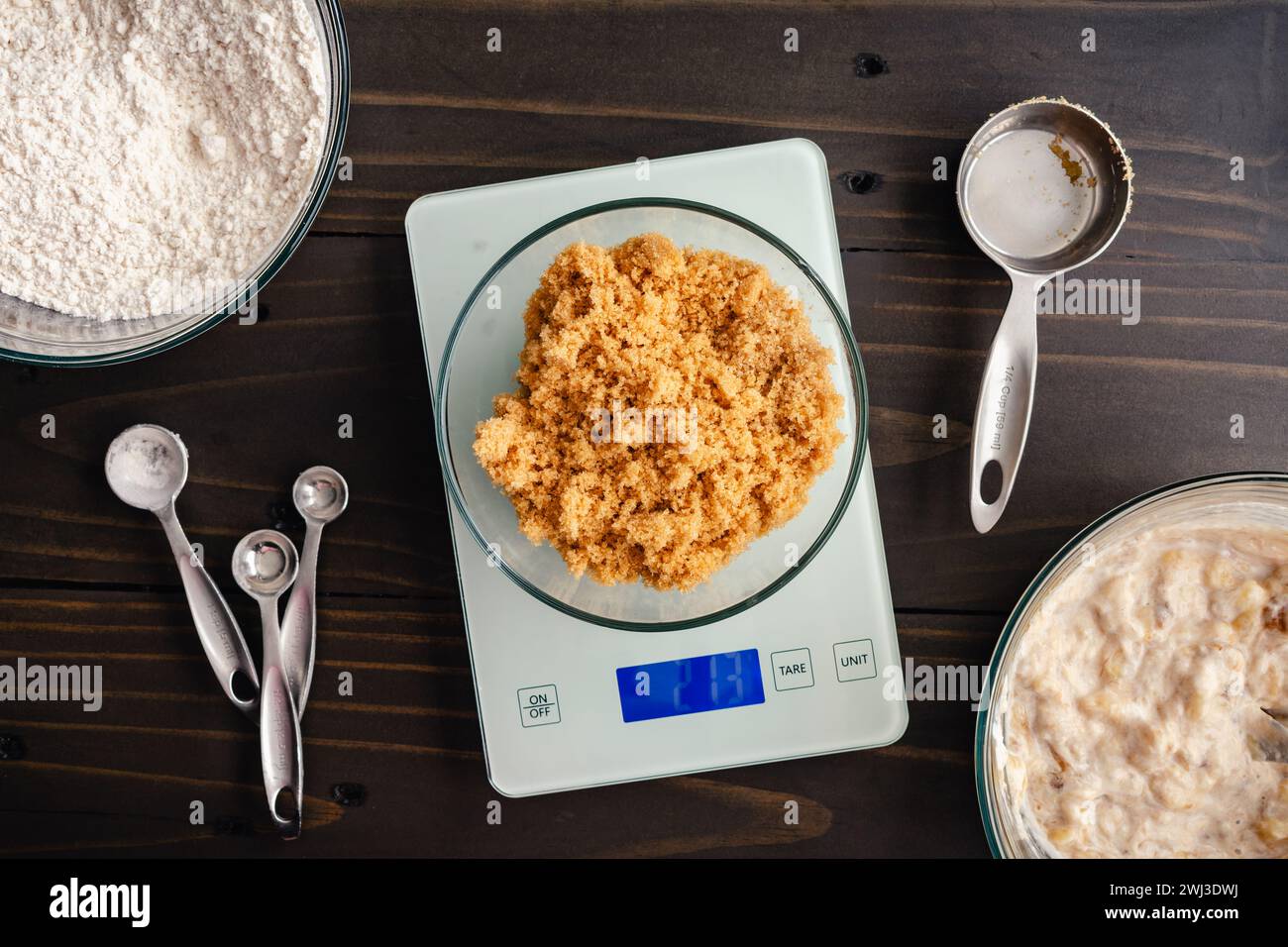 Heller brauner Zucker auf einer Küchenwaage wiegen: Brauner Zucker auf einer digitalen Waage mit nassen und trockenen Muffinzutaten an der Seite Stockfoto
