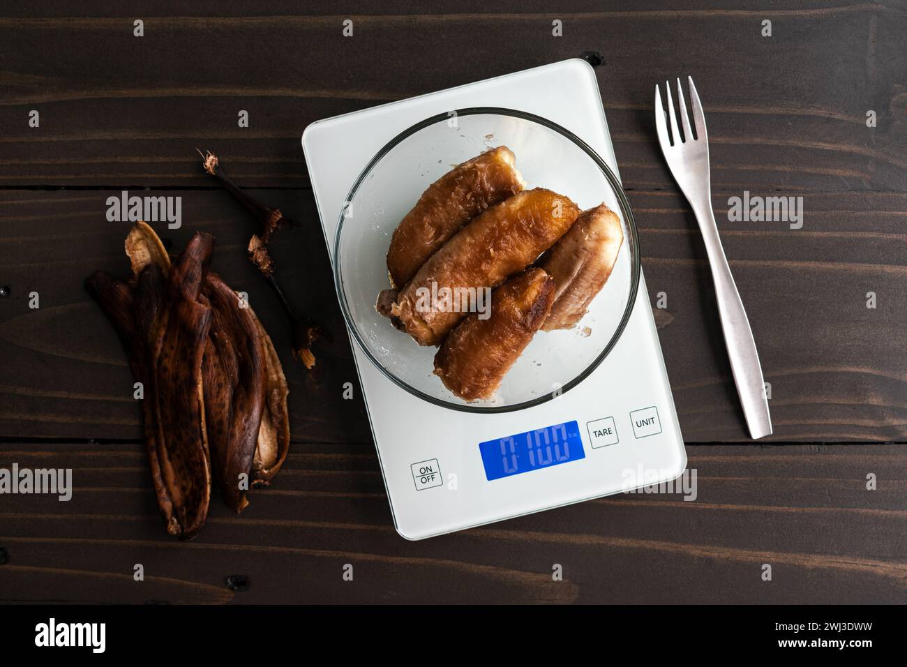 Wiegen geschälte überreife Bananen auf einer Küchenwaage: Glasschale mit sehr Reifen Bananen auf einer digitalen Waage mit Schalen und einer Gabel an der Seite Stockfoto