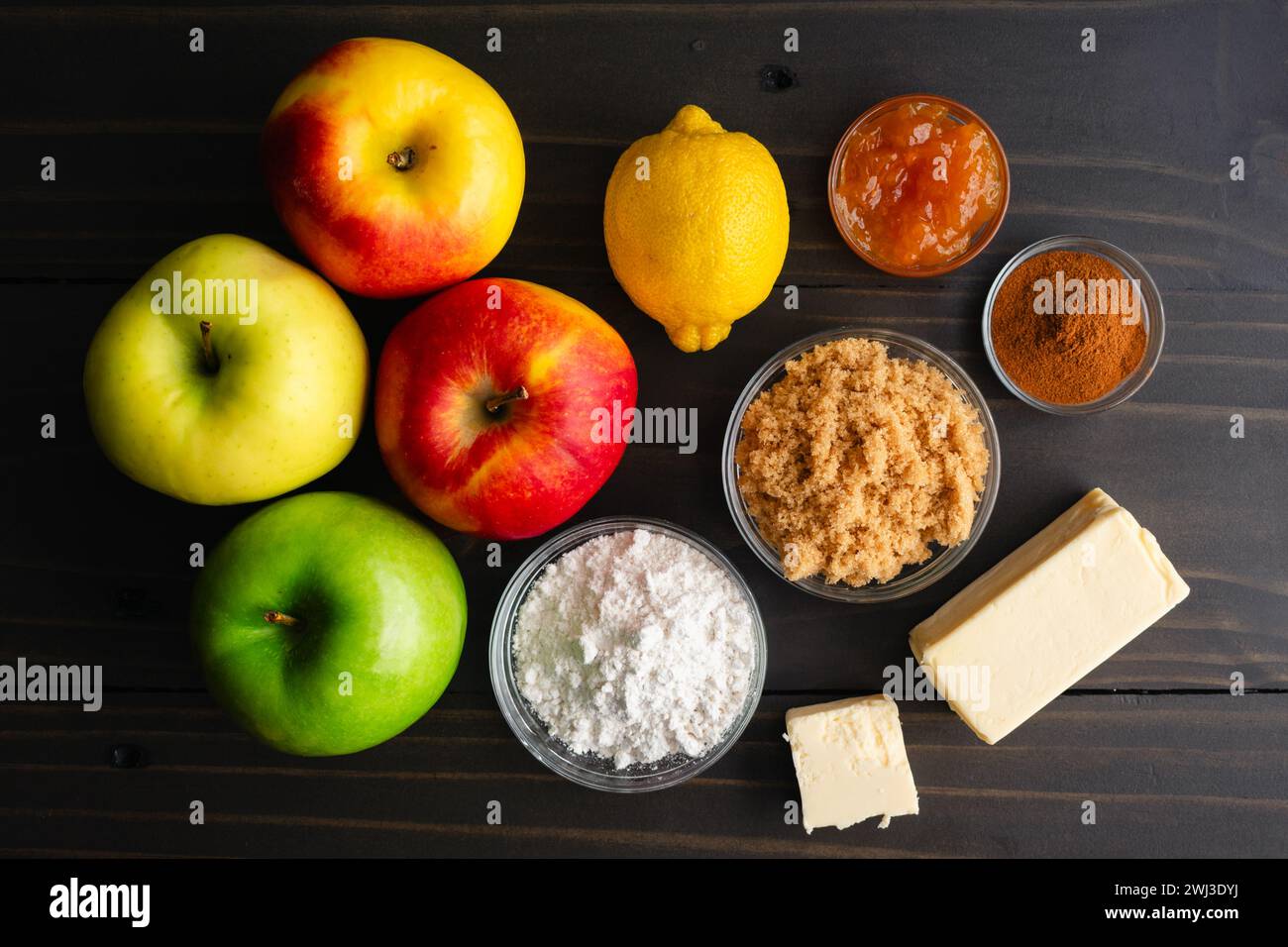 Vegane Apfeltorte Zutaten auf einem Holztisch: Frische Äpfel, Mehl, brauner Zucker, vegane Butter und andere Zutaten für Gebäck auf dunklem Hintergrund Stockfoto