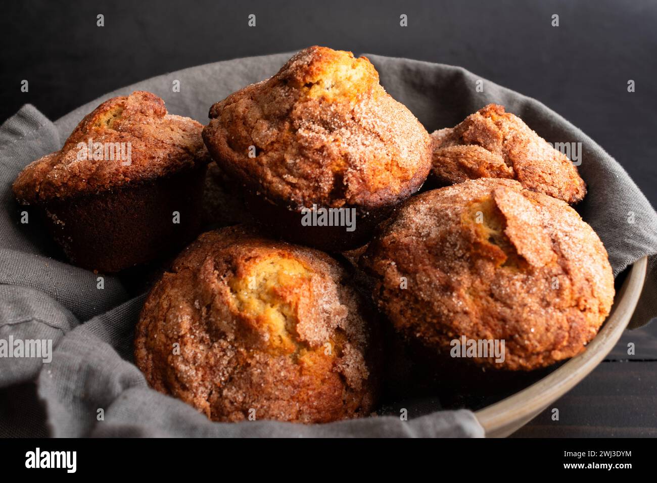Banana Cinnamon Muffins serviert in einer großen Schüssel: Nahaufnahme eines mit Leinenfutter gefüllten Korbs voller frisch gebackener Frühstückstümmffins Stockfoto