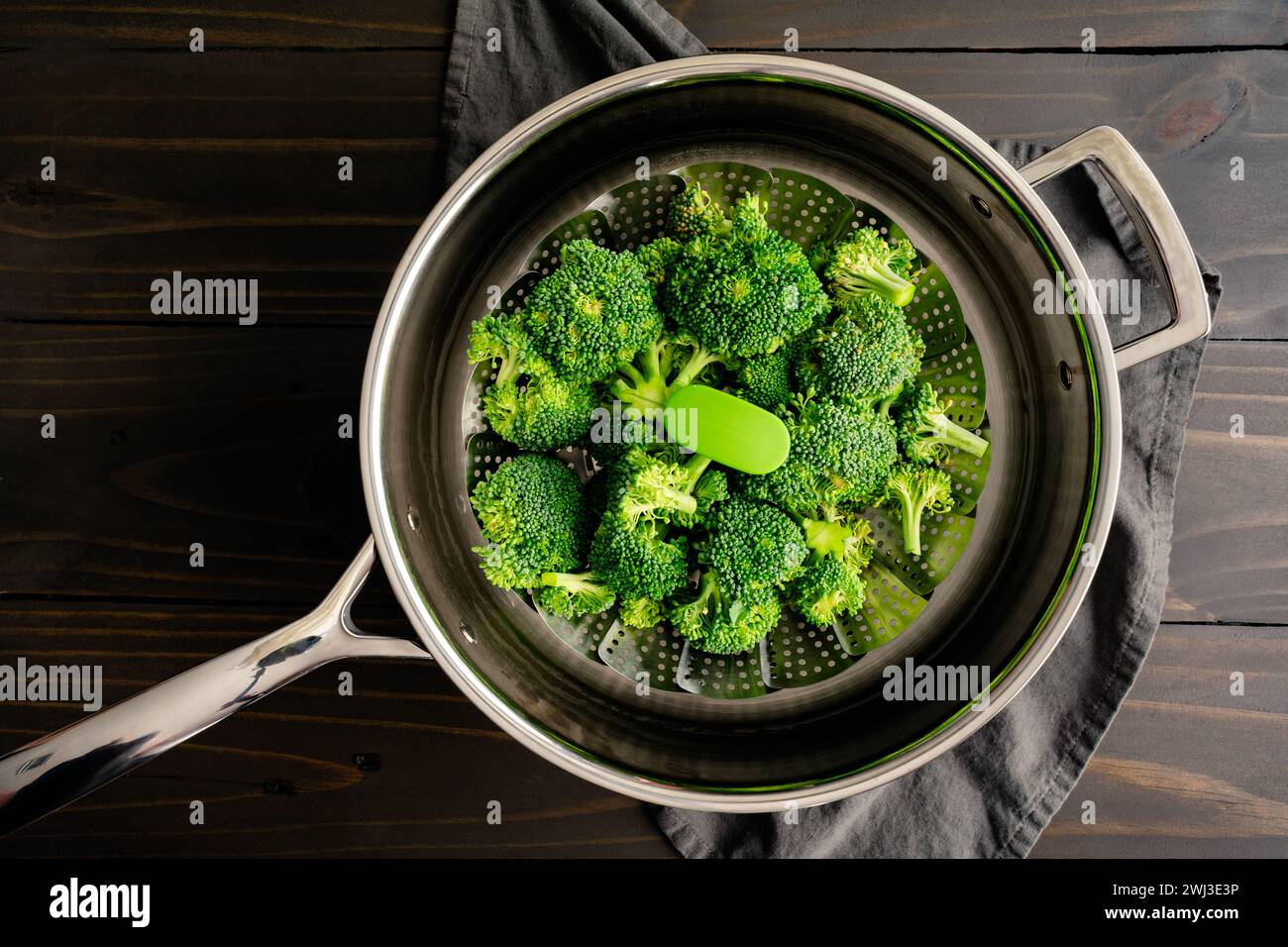 Brokkoli-Röschen auf einem Dampfkorb in einer Pfanne: Rohe Brokkoli-Röschen in einem zusammenklappbaren Dampfkorb aus Metall in einer Pfanne mit Wasser Stockfoto