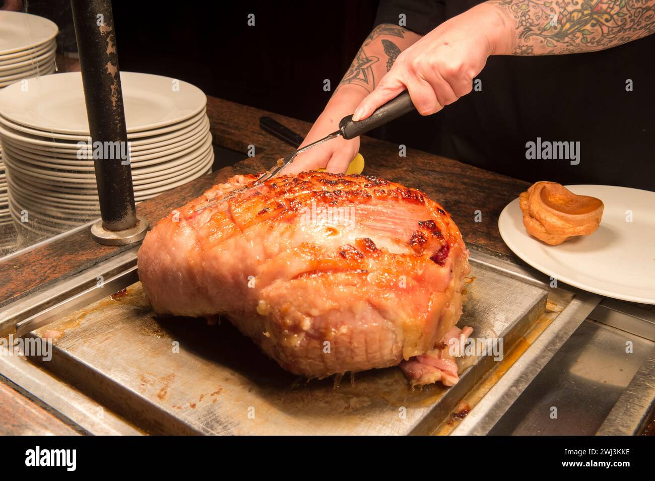 Ein Gammon-Gelenk wird in einem Pub von einem Mann mit Tätowierungen am Arm geschnitzt. Stockfoto