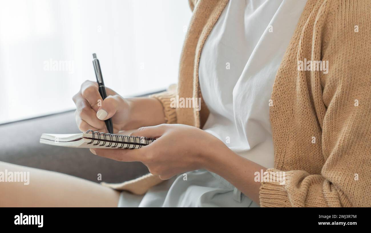 Asiatische Geschäftsfrau, die vom Büro aus arbeitet, liest und schreibt Notizen in Notizblock Stockfoto