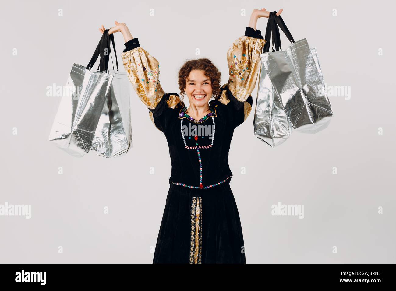 Junge Erwachsene Frau in einem mittelalterlichen Kleid gekleidet, die Einkaufstaschen in den Händen hält isolierter weißer Hintergrund. Stockfoto