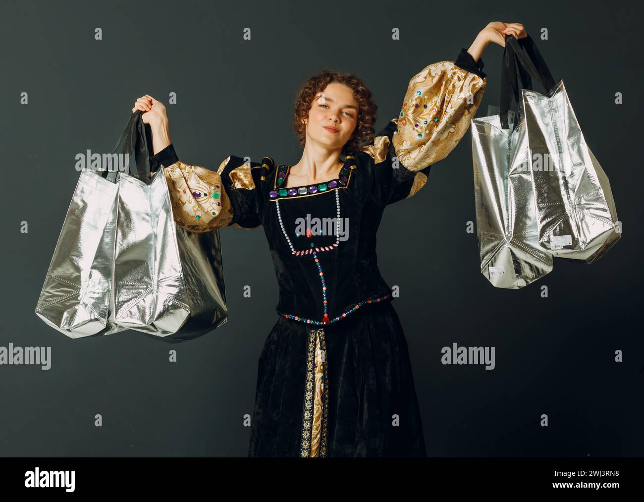 Junge Erwachsene Frau in einem mittelalterlichen Kleid, die Einkaufstaschen in den Händen hält Stockfoto