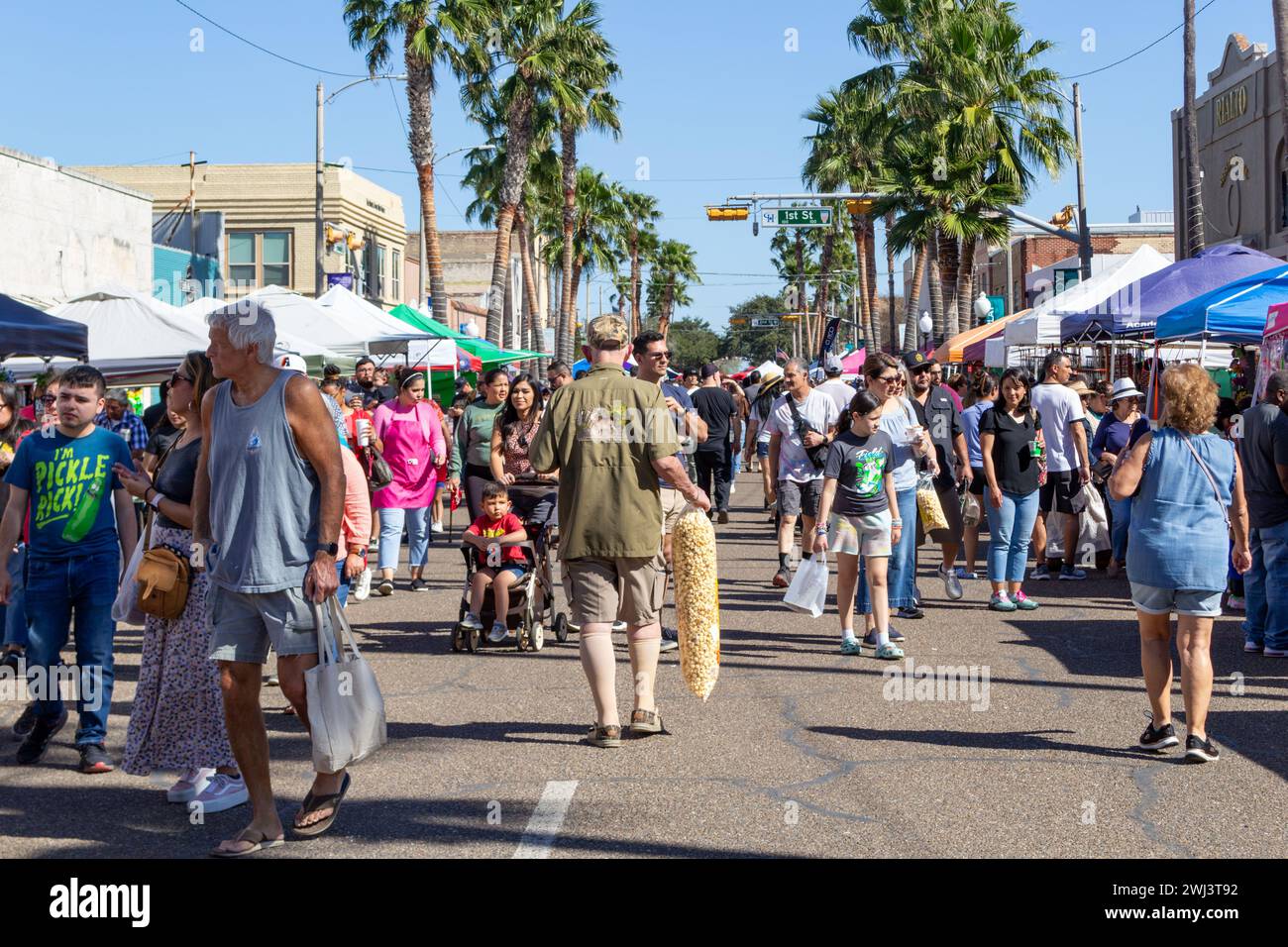Die Menschenmenge läuft eine Straße entlang, die von Verkäufern gesäumt ist, für den Harlingen Markt geschlossen, Mann in der Mitte mit einer großen Tüte Kessel Mais, Harlingen, Texas, USA. Stockfoto