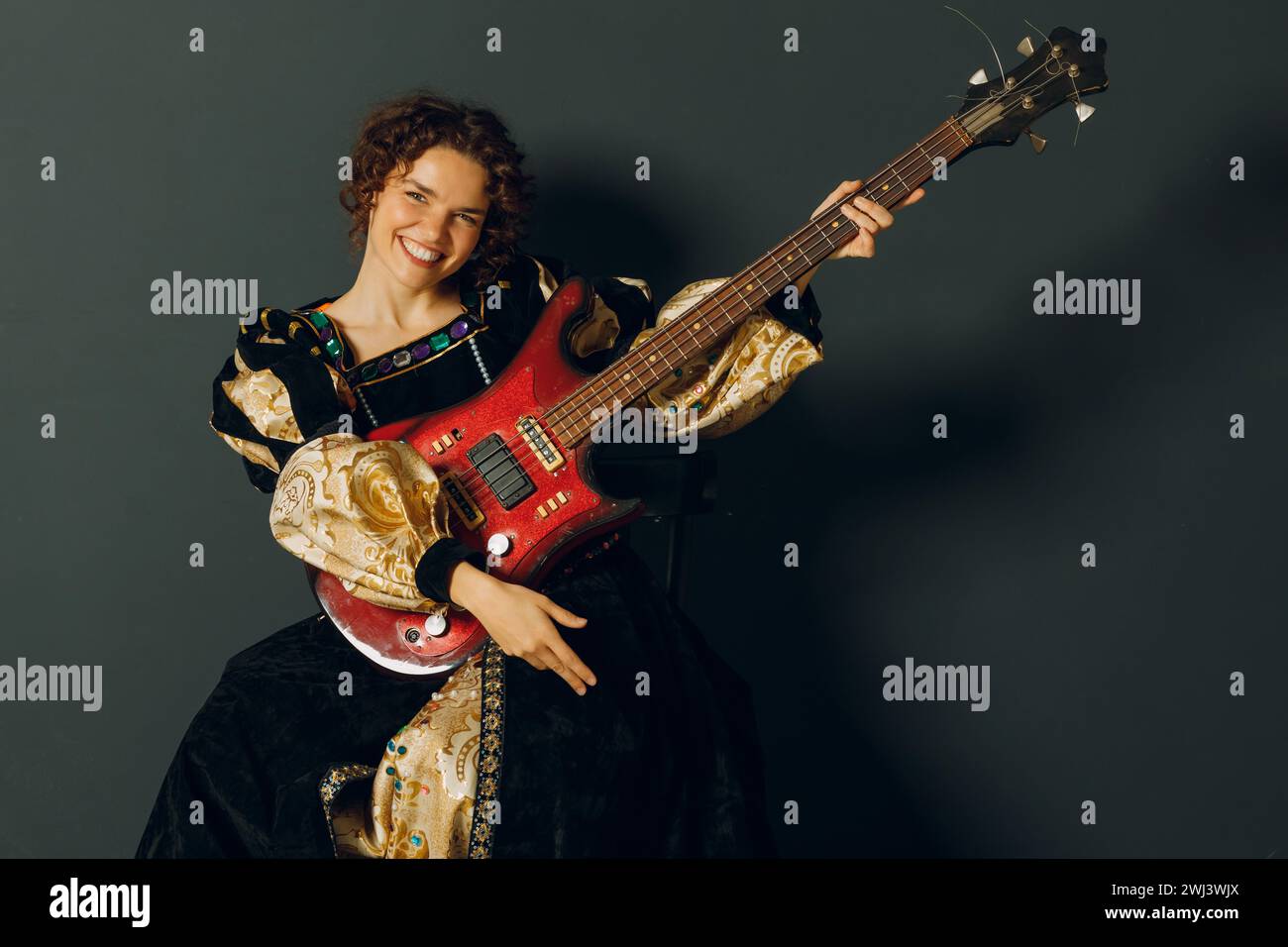 Porträt einer jungen erwachsenen Frau, die Musik auf elektrischer Gitarre spielt und in einem mittelalterlichen Kleid gekleidet ist. Stockfoto