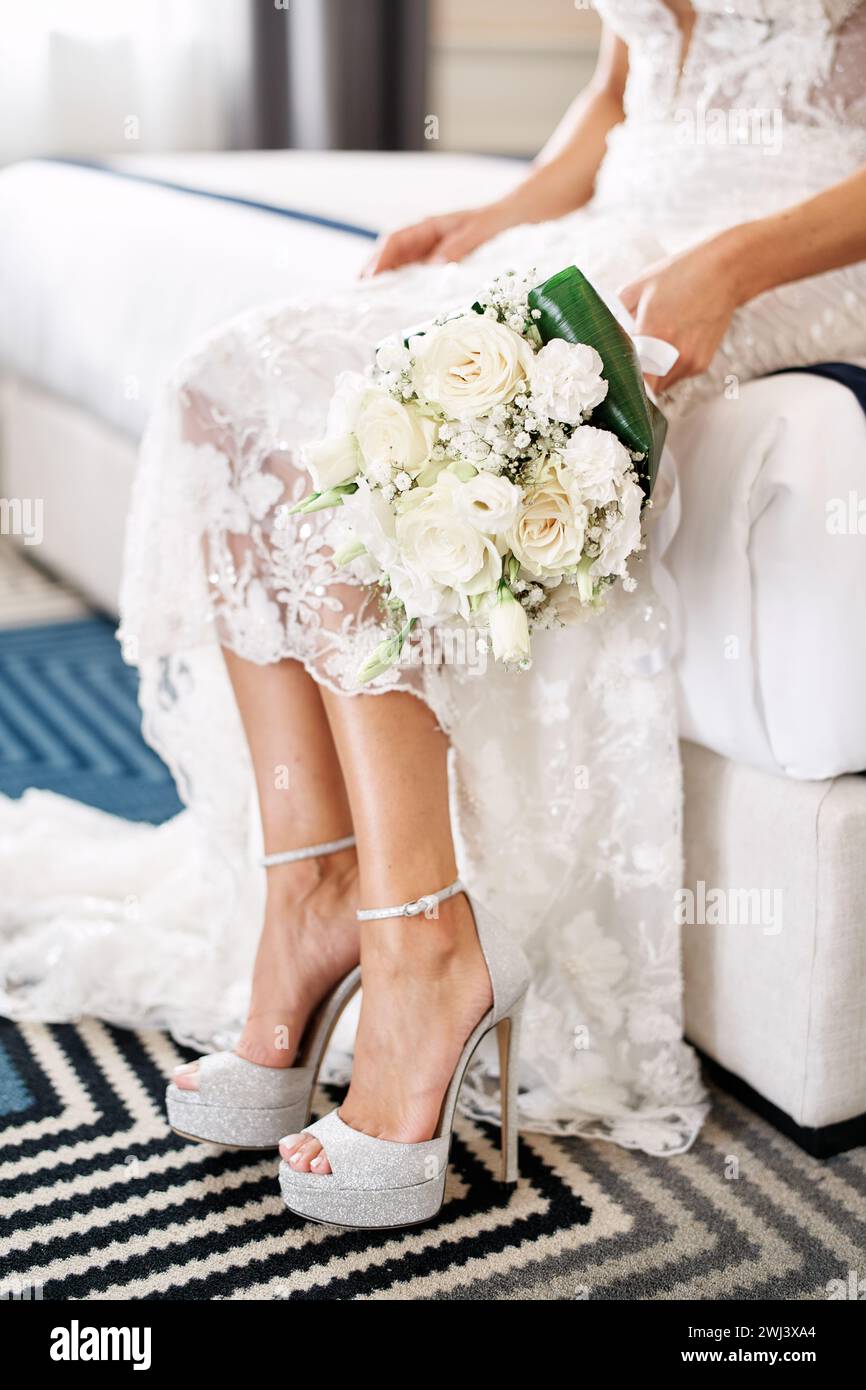 Braut mit einem Blumenstrauß sitzt auf dem Bett. Abgeschnitten. Gesichtslos Stockfoto