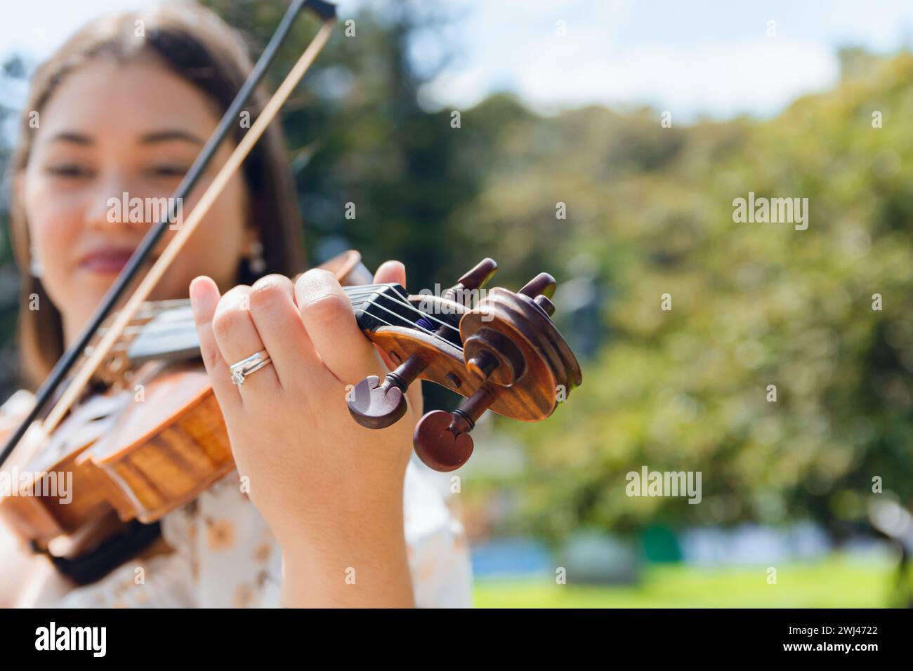 Nahaufnahme des Weitwinkelbildes einer unscharfen lateinischen jungen Buskerin, die im Freien Geige spielt, Fokus auf den Geigenhals und die Muschel mit klarem Himmel im Hintergrund Stockfoto