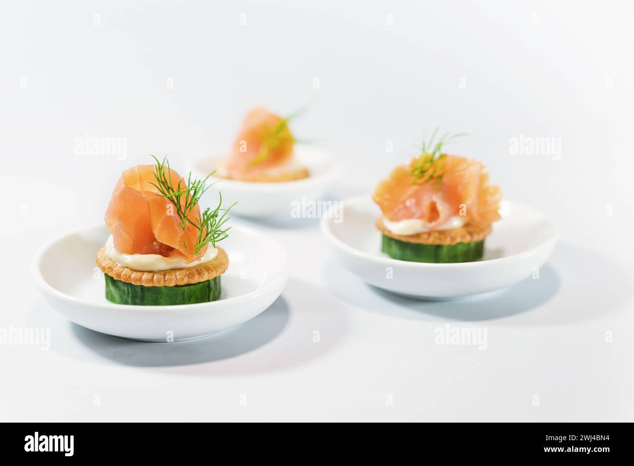 Kanapees als Party Fingerfood für das kalte Buffet aus Gurke, Crackern, Frischkäse, Räucherlachs und Dill auf kleinem Weißwein Stockfoto