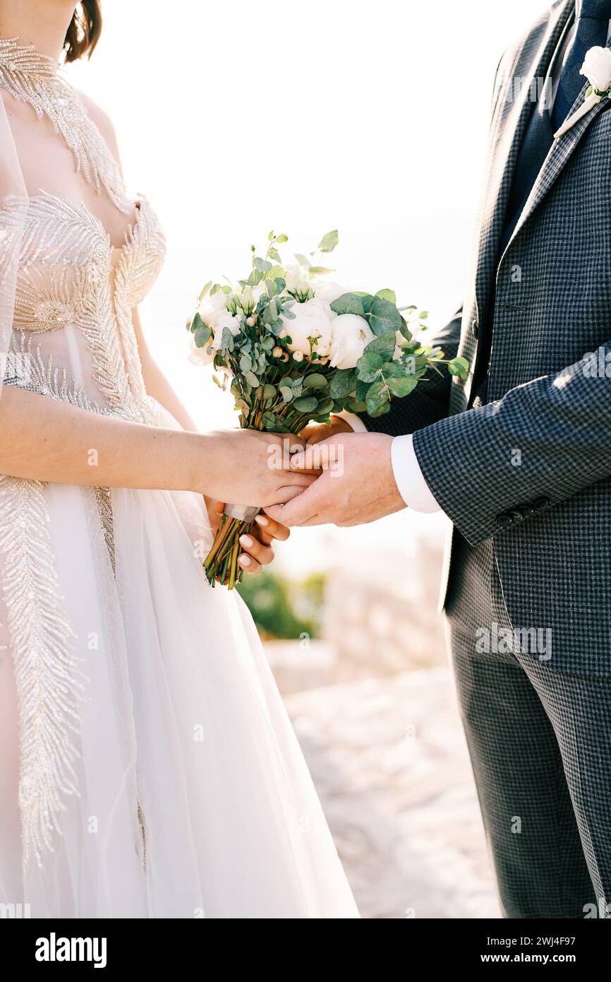 Der Bräutigam hält die Hände der Braut mit einem Blumenstrauß. Abgeschnitten. Gesichtslos Stockfoto