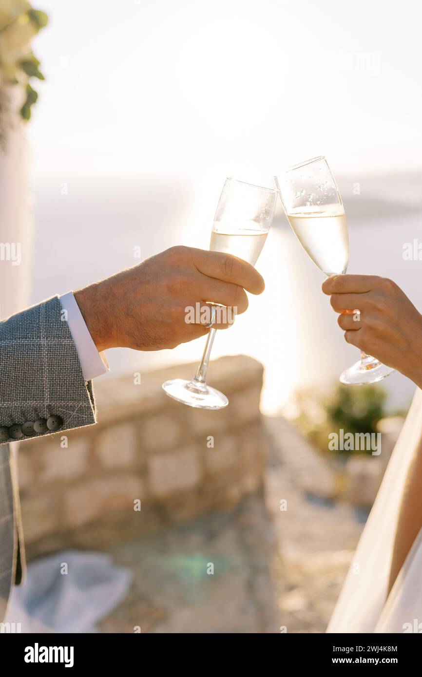 Braut und Bräutigam zwitschern vor dem Hintergrund eines sonnigen Himmels Gläser Champagner. Abgeschnitten. Gesichtslos Stockfoto