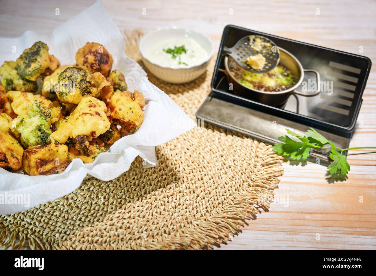 Frittierter Blumenkohl und Brokkoli in Bierteig, bereit zum Verzehr auf einem Holztisch und einem Smartphone, das zeigt, wie man den Rezept kocht Stockfoto