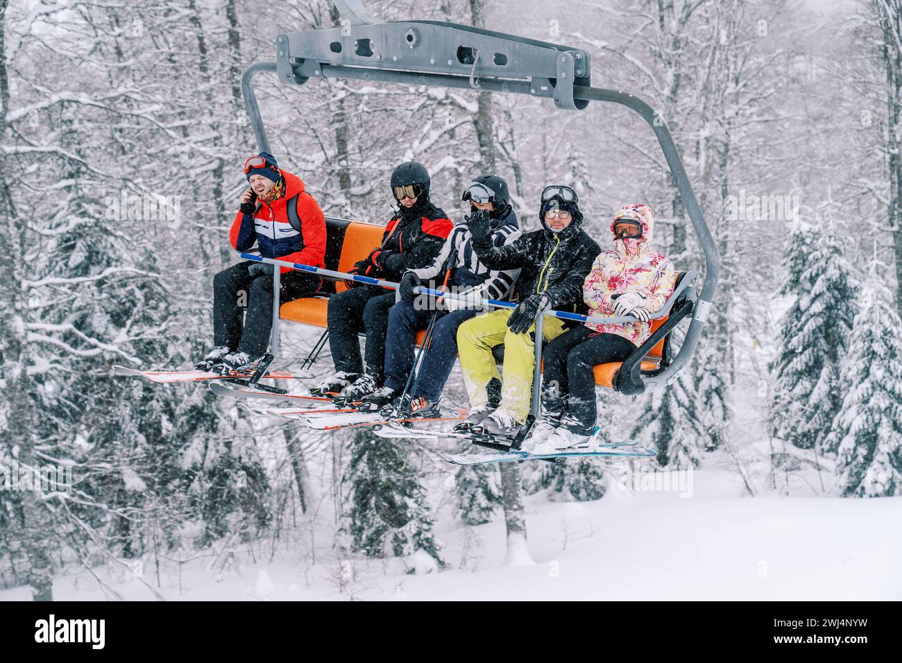 Skifahrer in hellen Skianzügen fahren eine verschneite Piste auf einem Skilift hinauf Stockfoto