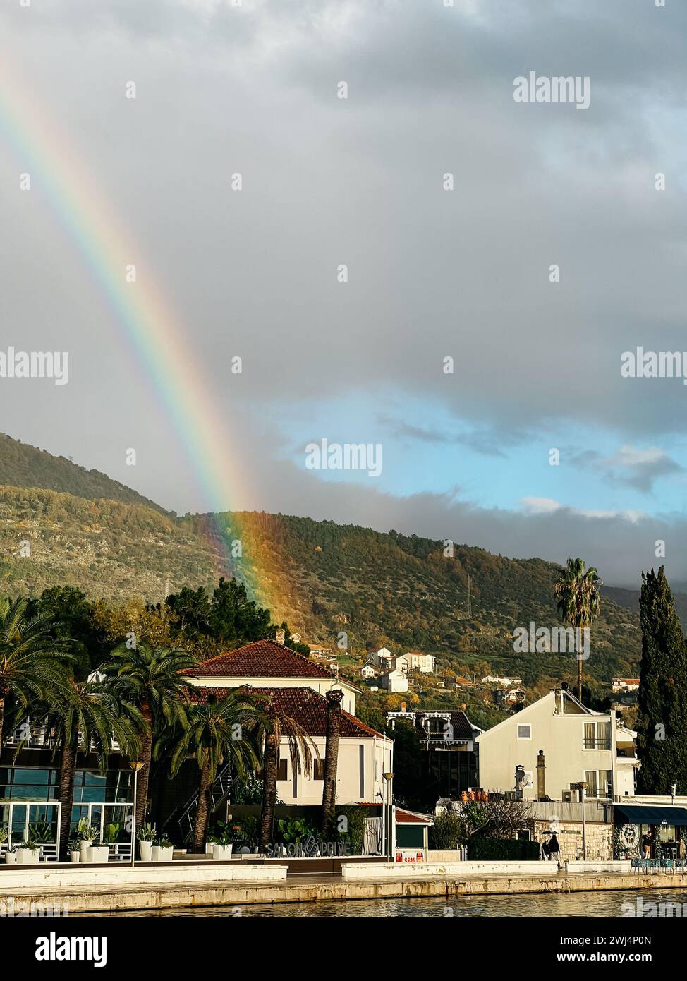 Farbenfroher Regenbogen über den Häusern an der Küste am Fuße der Berge Stockfoto