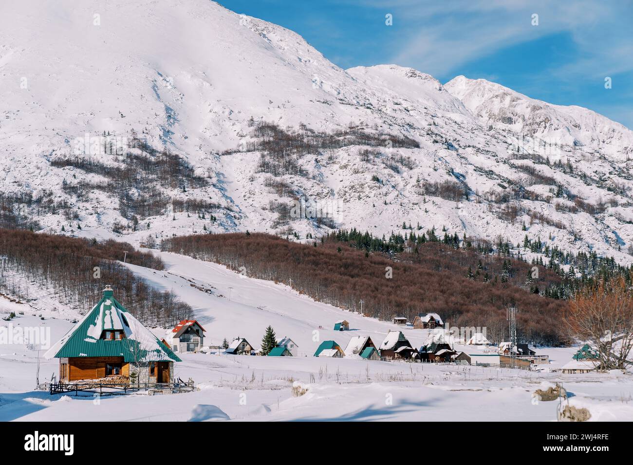 Gemütliches Holzhaus in einem Dorf am Fuße schneebedeckter bewaldeter Berge Stockfoto