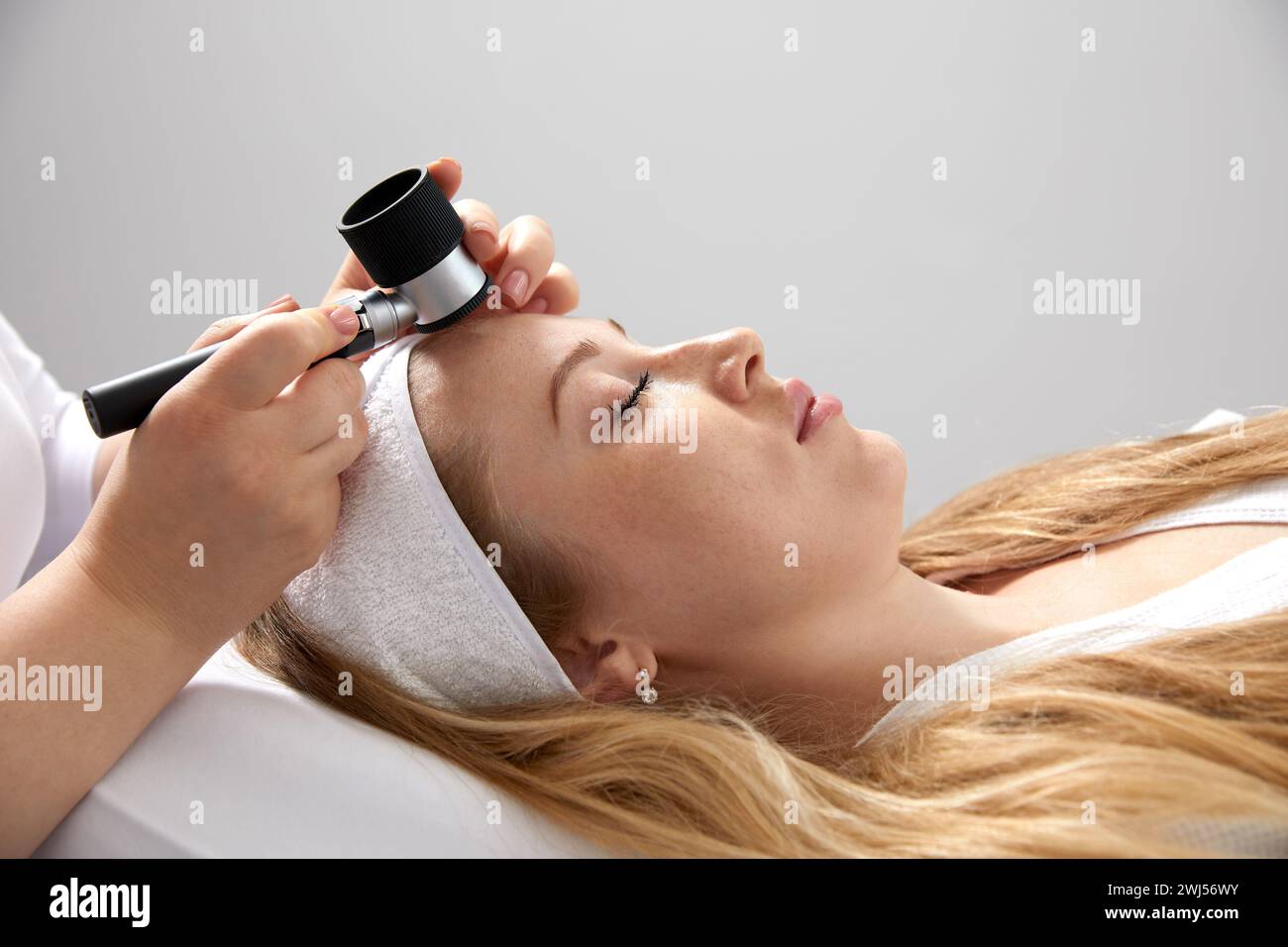 Frau bekommt eine professionelle Hautuntersuchung in der Arztpraxis. Dermatologe oder Kosmetikspezialist verwendet Vergrößerungsglas, um Untersuchungen durchzuführen Stockfoto