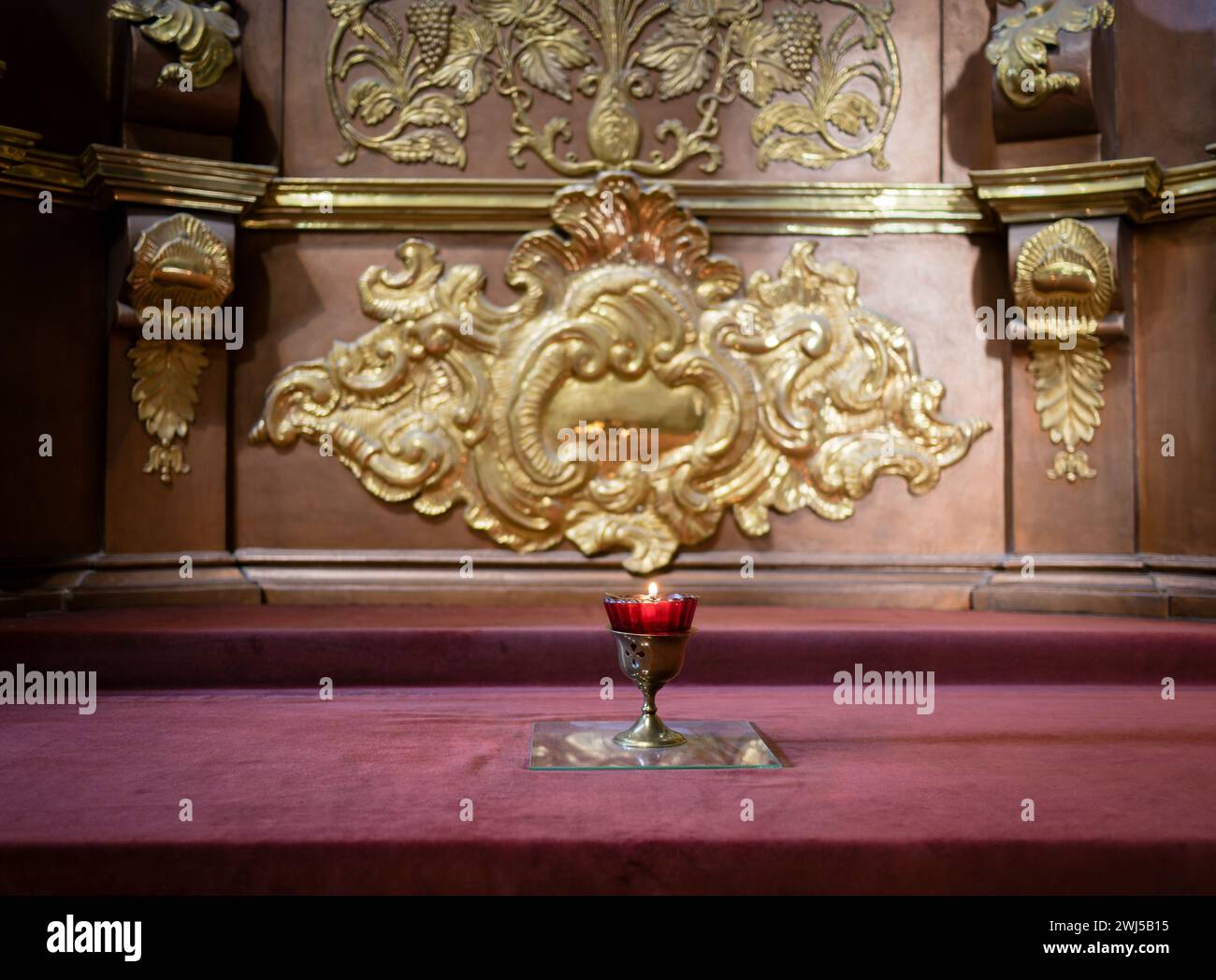 Brennende Kerze auf einem Silberständer mit einem geschnitzten Kreuz. Hintergrund Stockfoto