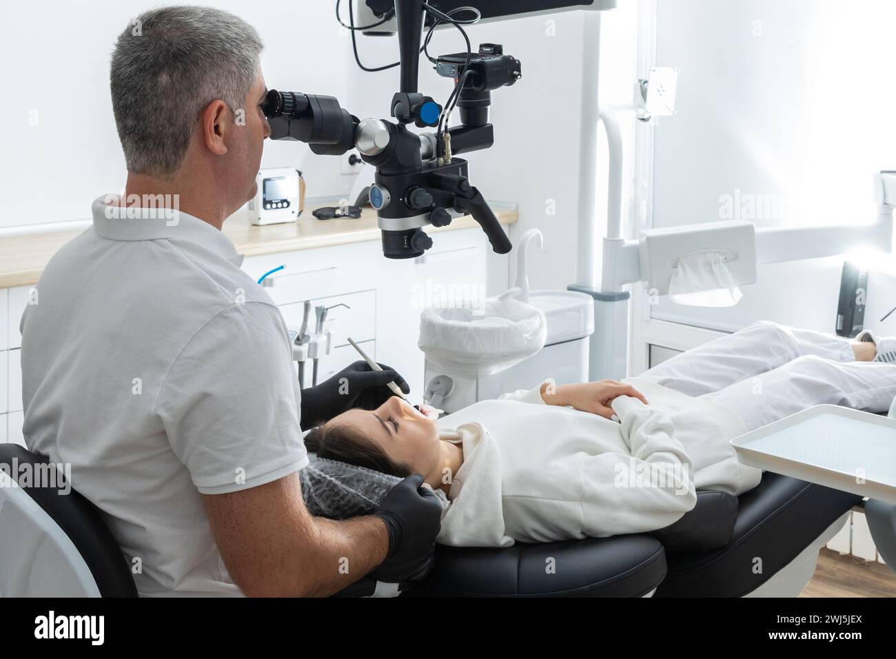 Zahnarzt mit Zahnmikroskop zur Behandlung von Patientenzähnen in der zahnärztlichen Klinik. Medizin, Zahnheilkunde und Gesundheitskonzept. Den Stockfoto