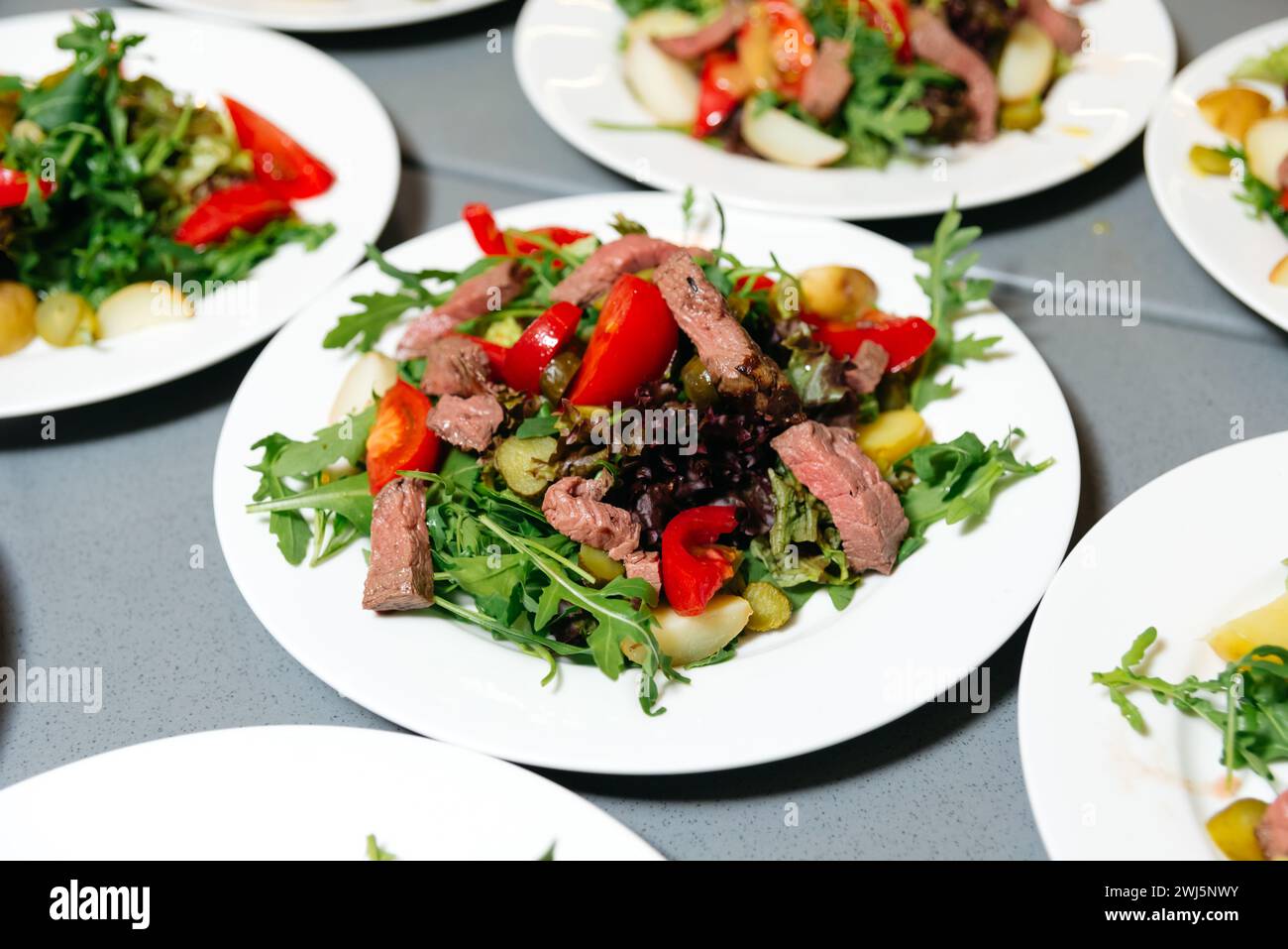 Frischer Rindersalat mit Gemüse auf Teller. Ein gesunder Rindersalat mit Rucola, roter Paprika und gemischtem Gemüse, serviert auf einem weißen Teller. Stockfoto