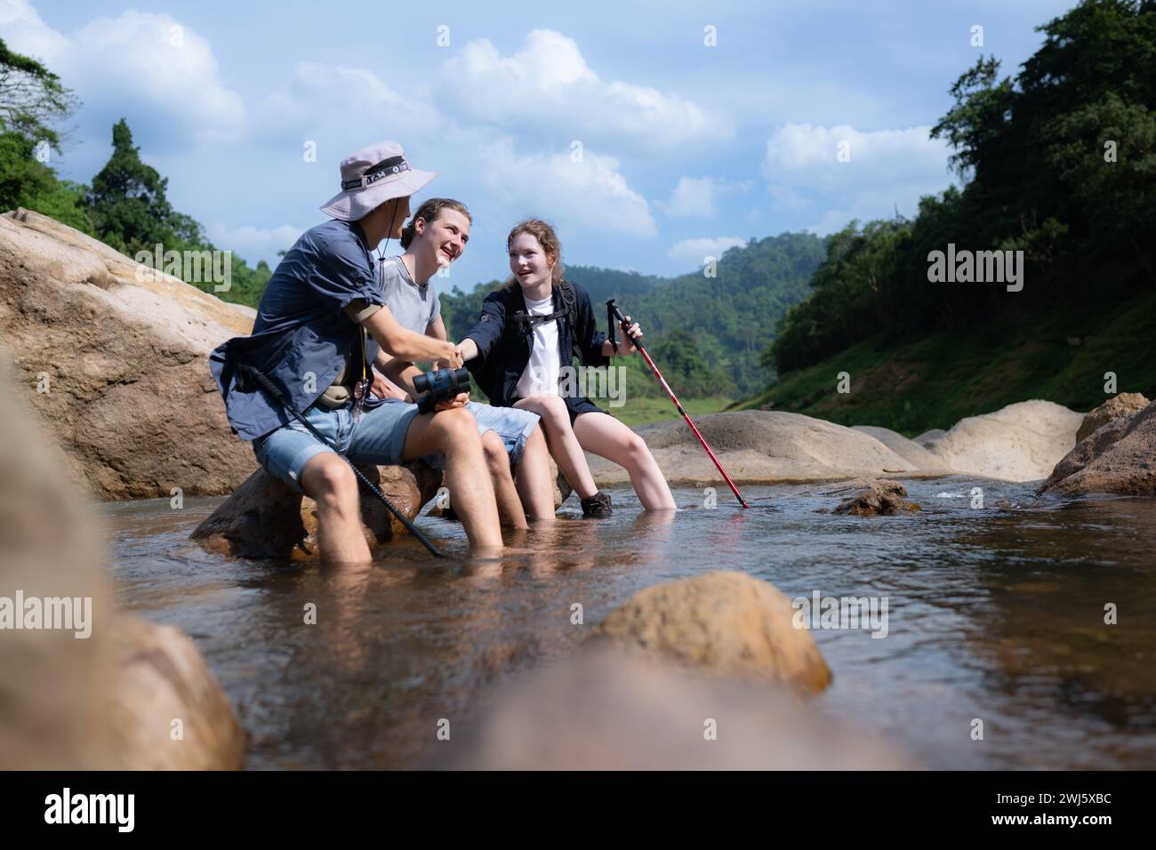 Gruppe von Freunden, die auf dem Felsen in der Mitte des Flusses sitzen. Ruhen Sie sich während der Wanderung im Wald aus. Stockfoto