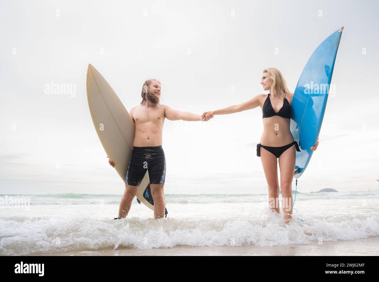 Ein paar Surfer halten Hände und schauen sich am Strand an Stockfoto