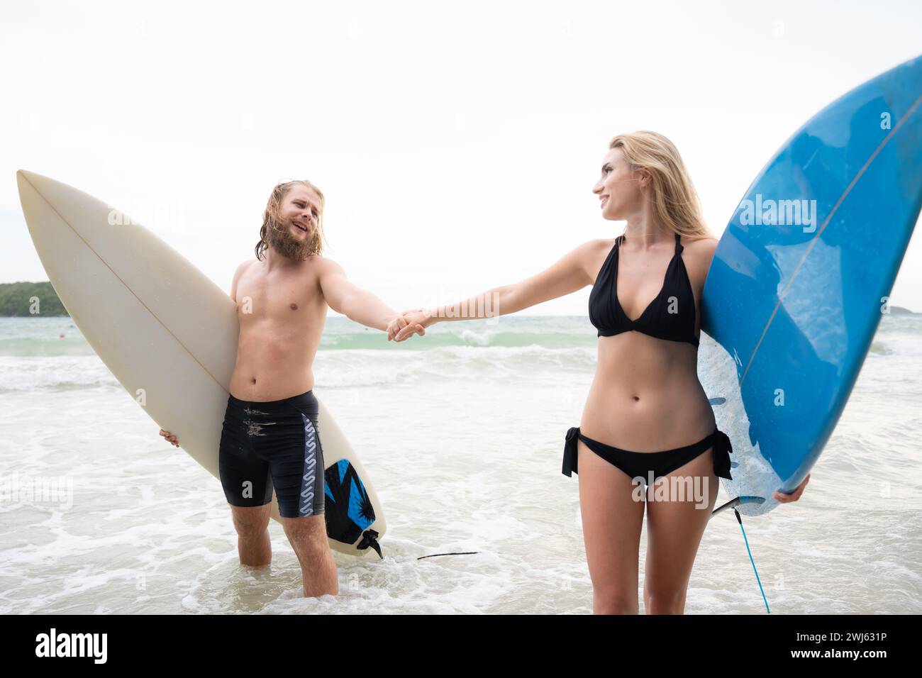 Ein paar Surfer halten Hände und schauen sich am Strand an Stockfoto