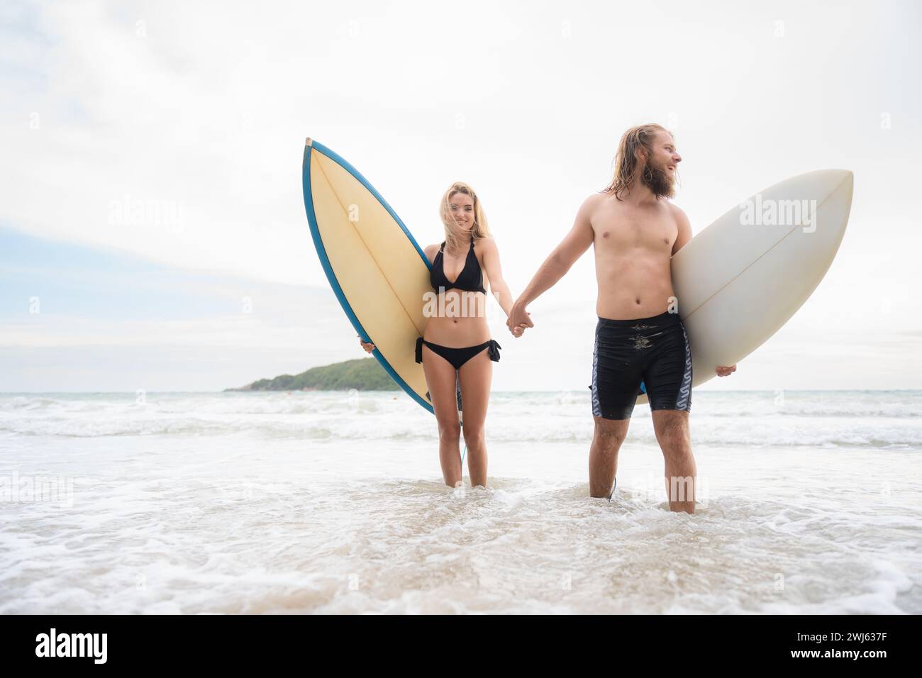 Ein paar Surfer halten Hände und schauen sich am Strand an Stockfoto