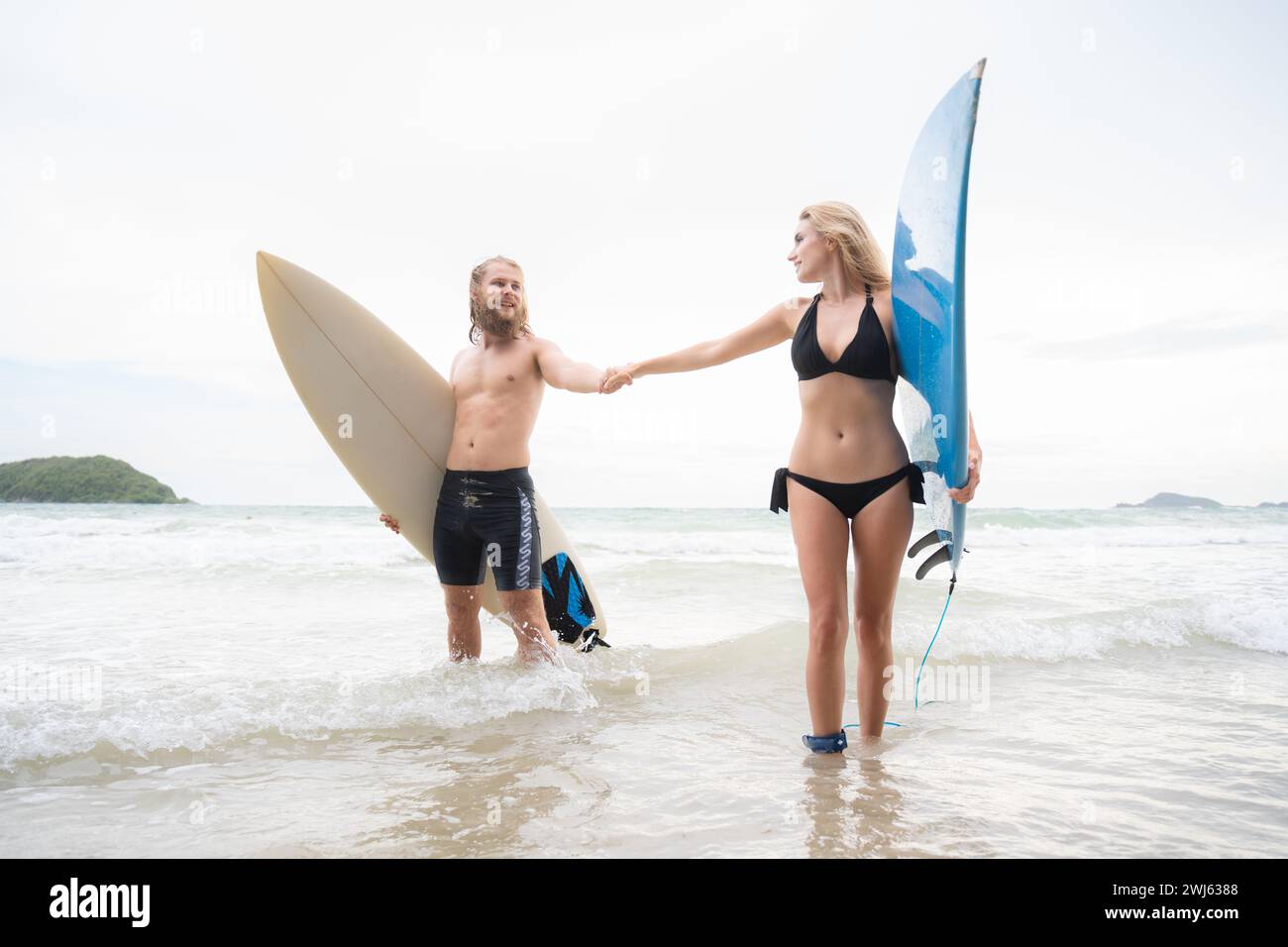 Ein paar Surfer halten Hände und schauen sich am Strand an Stockfoto