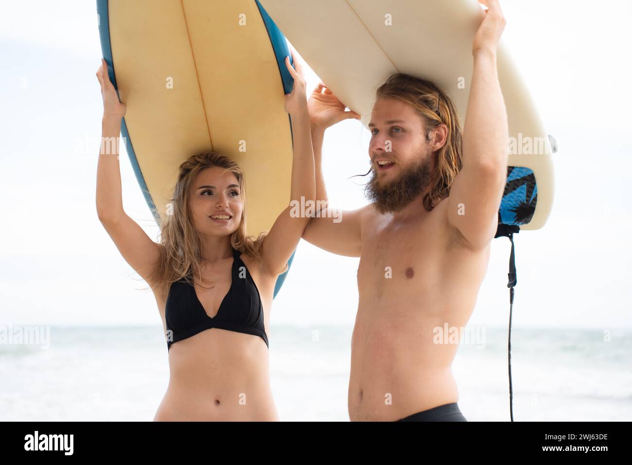 Junge Männer und Frauen halten Surfbretter auf dem Kopf und gehen ins Meer, um zu surfen Stockfoto