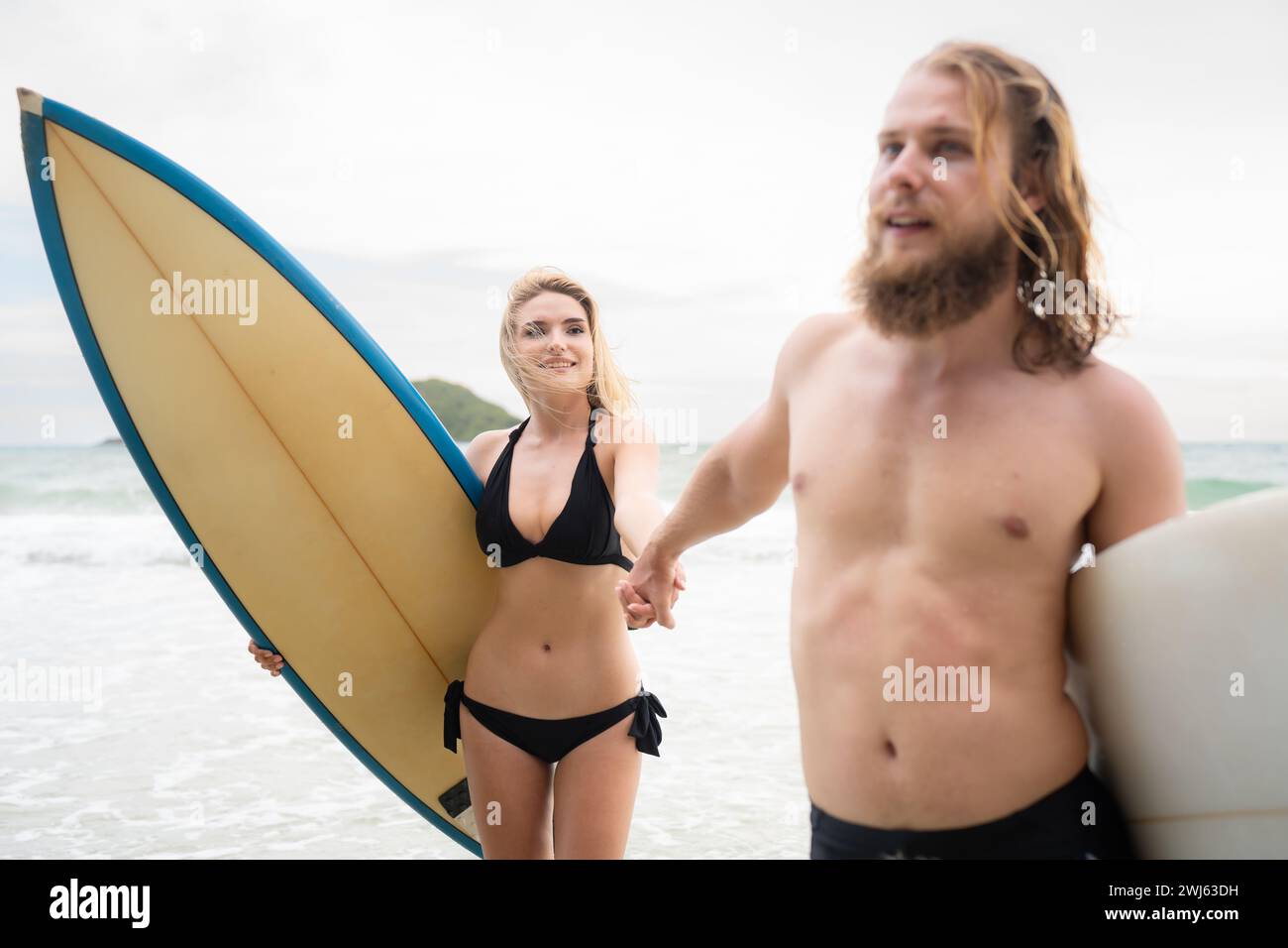 Ein paar Surfer halten Hände und schauen sich am Strand an Stockfoto