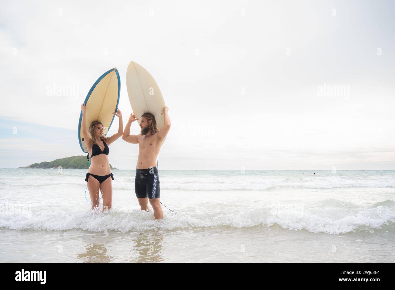 Junge Männer und Frauen halten Surfbretter auf dem Kopf und gehen ins Meer, um zu surfen Stockfoto