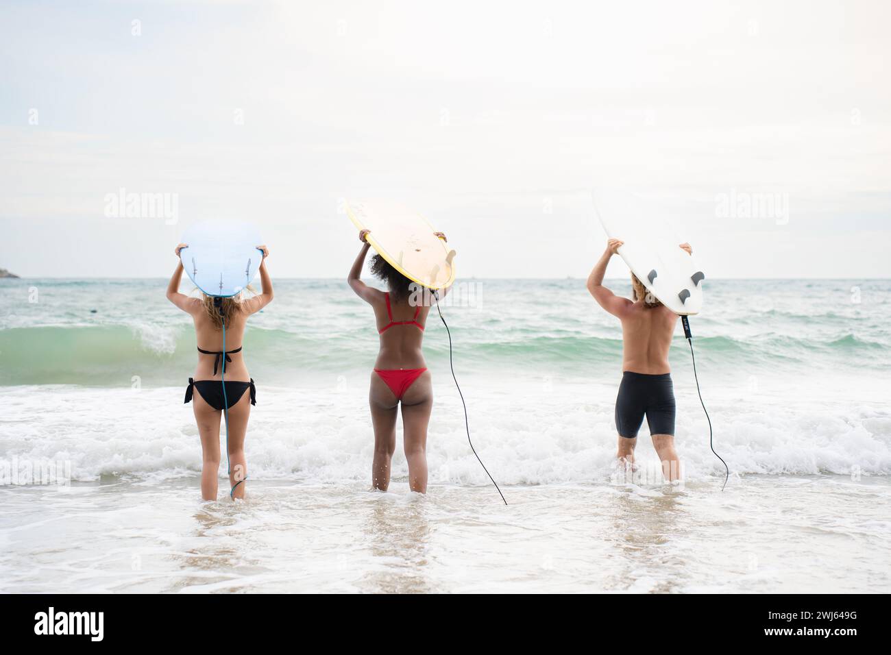 Rückansicht von zwei Frauen und jungen Männern, die Surfbretter auf dem Kopf halten und zum Surfen ins Meer gehen Stockfoto