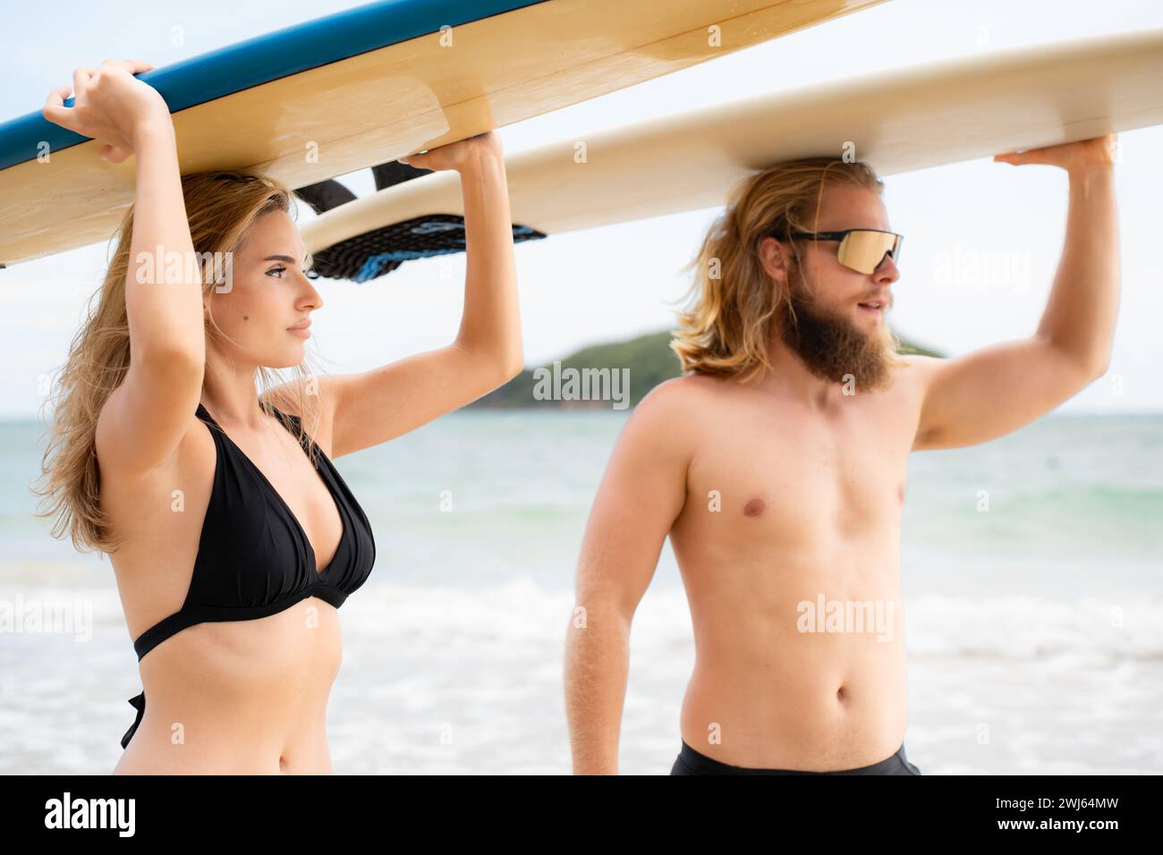 Junge Männer und Frauen halten Surfbretter auf dem Kopf und gehen ins Meer, um zu surfen Stockfoto