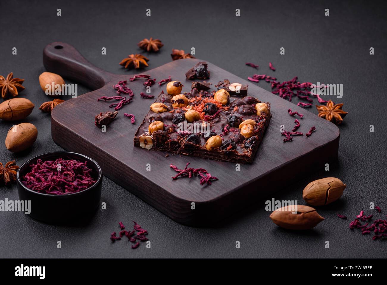 Handgemachte Schokolade mit Beeren, Nüssen und Gewürzen auf dunklem Hintergrund Stockfoto