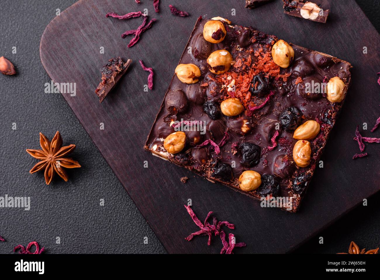 Handgemachte Schokolade mit Beeren, Nüssen und Gewürzen auf dunklem Hintergrund Stockfoto