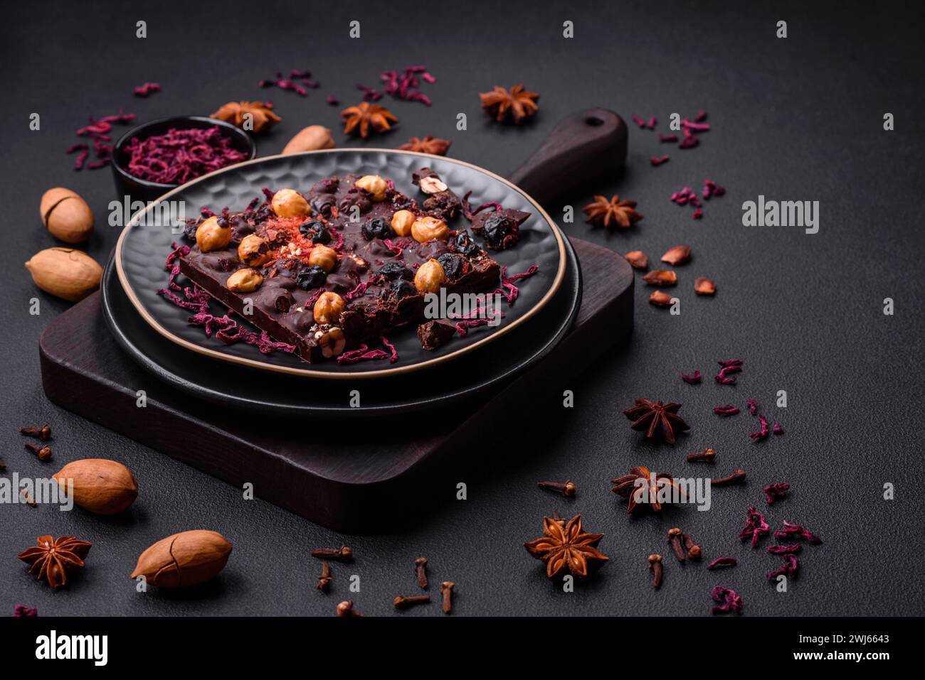 Handgemachte Schokolade mit Beeren, Nüssen und Gewürzen auf dunklem Hintergrund Stockfoto