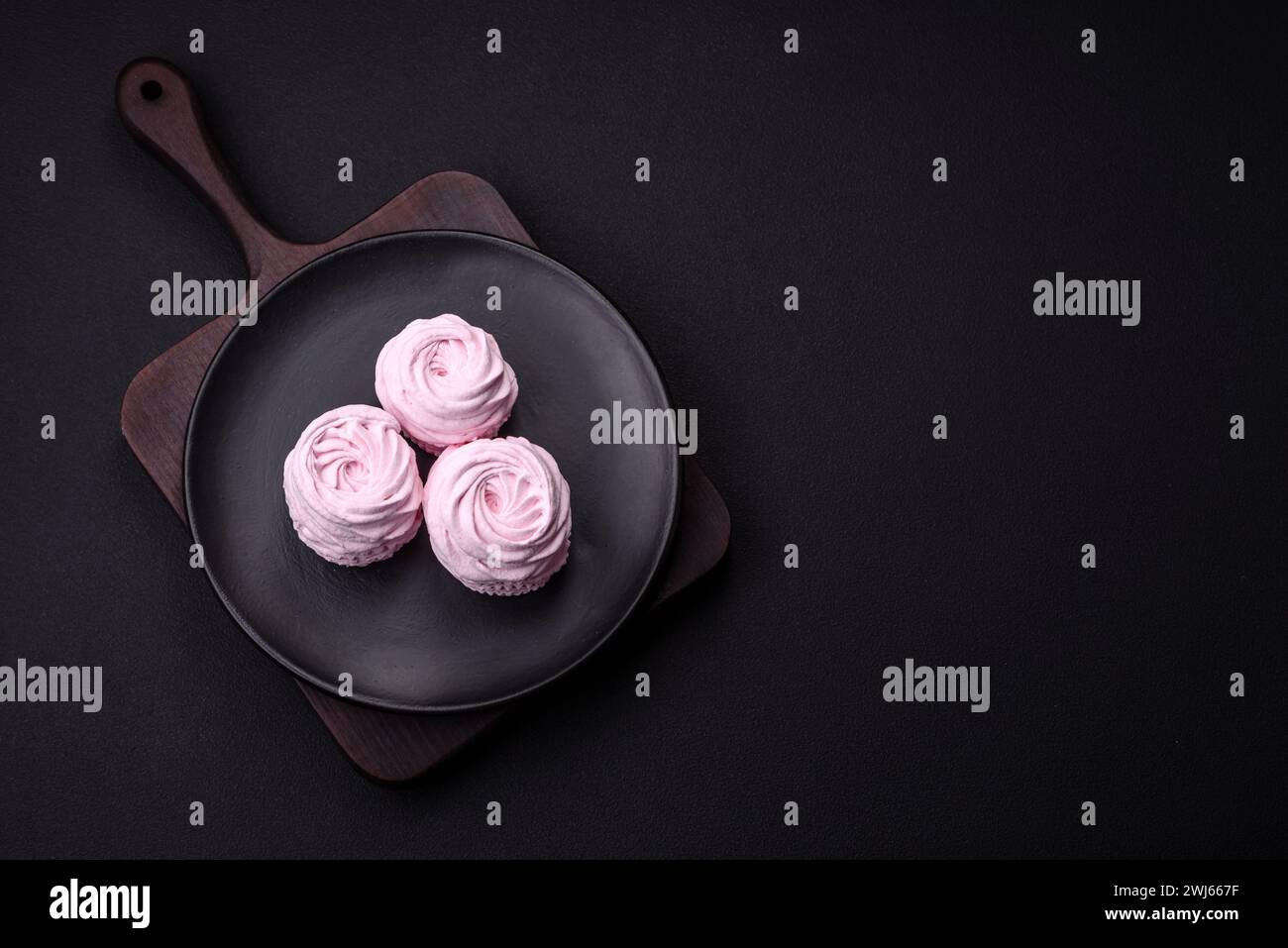 Köstliche frische, natürliche Marshmallows auf schwarzer Keramikplatte auf dunklem Betonhintergrund Stockfoto