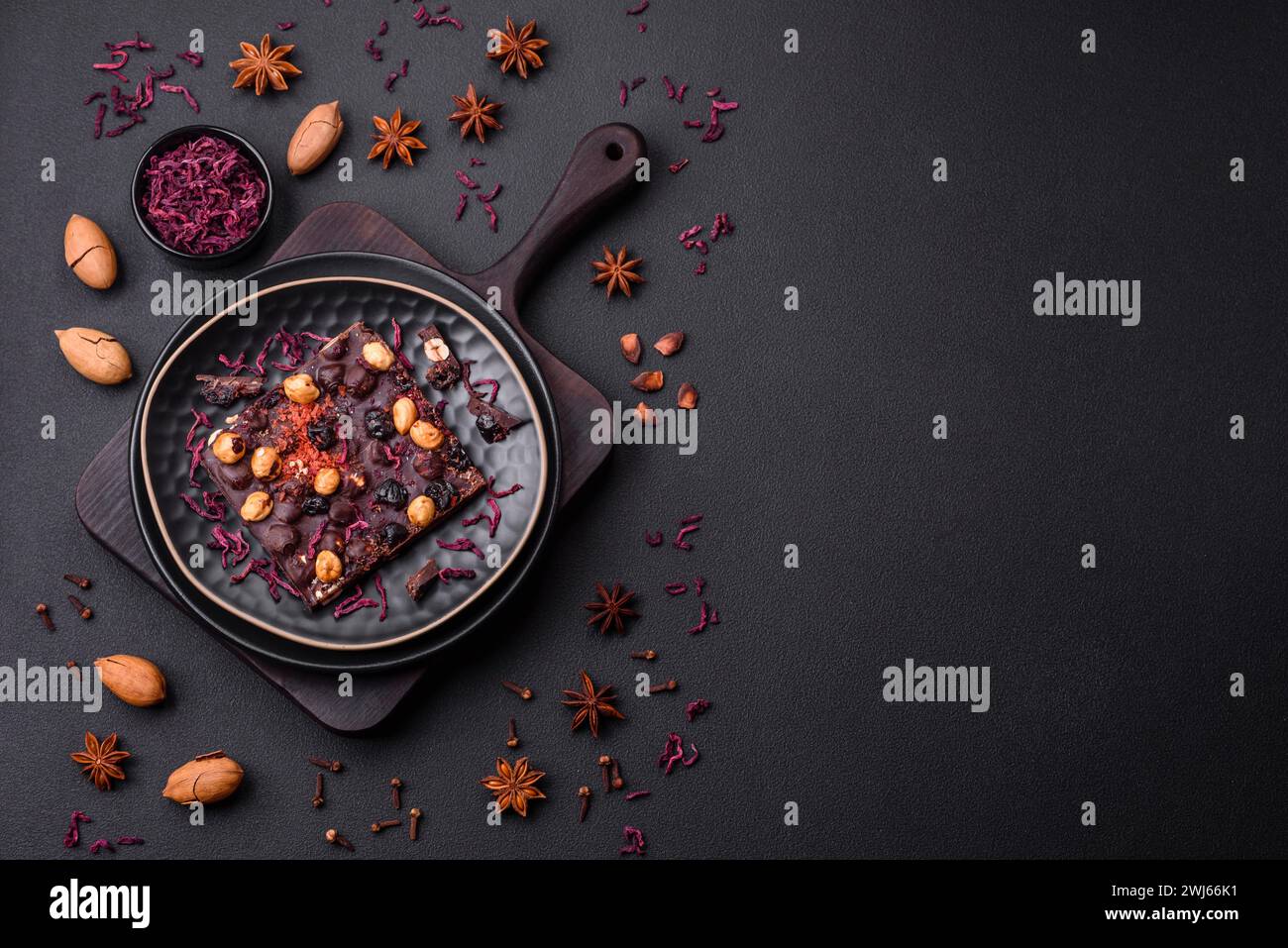 Handgemachte Schokolade mit Beeren, Nüssen und Gewürzen auf dunklem Hintergrund Stockfoto