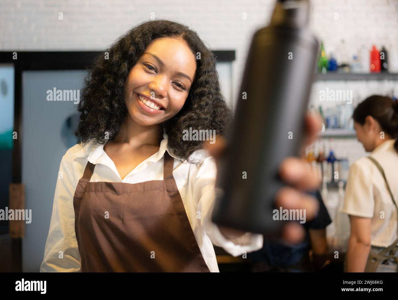 Der Barista für junge Frauen serviert Gäste, die ihre eigenen Tassen in einem Café mitbringen. Stockfoto