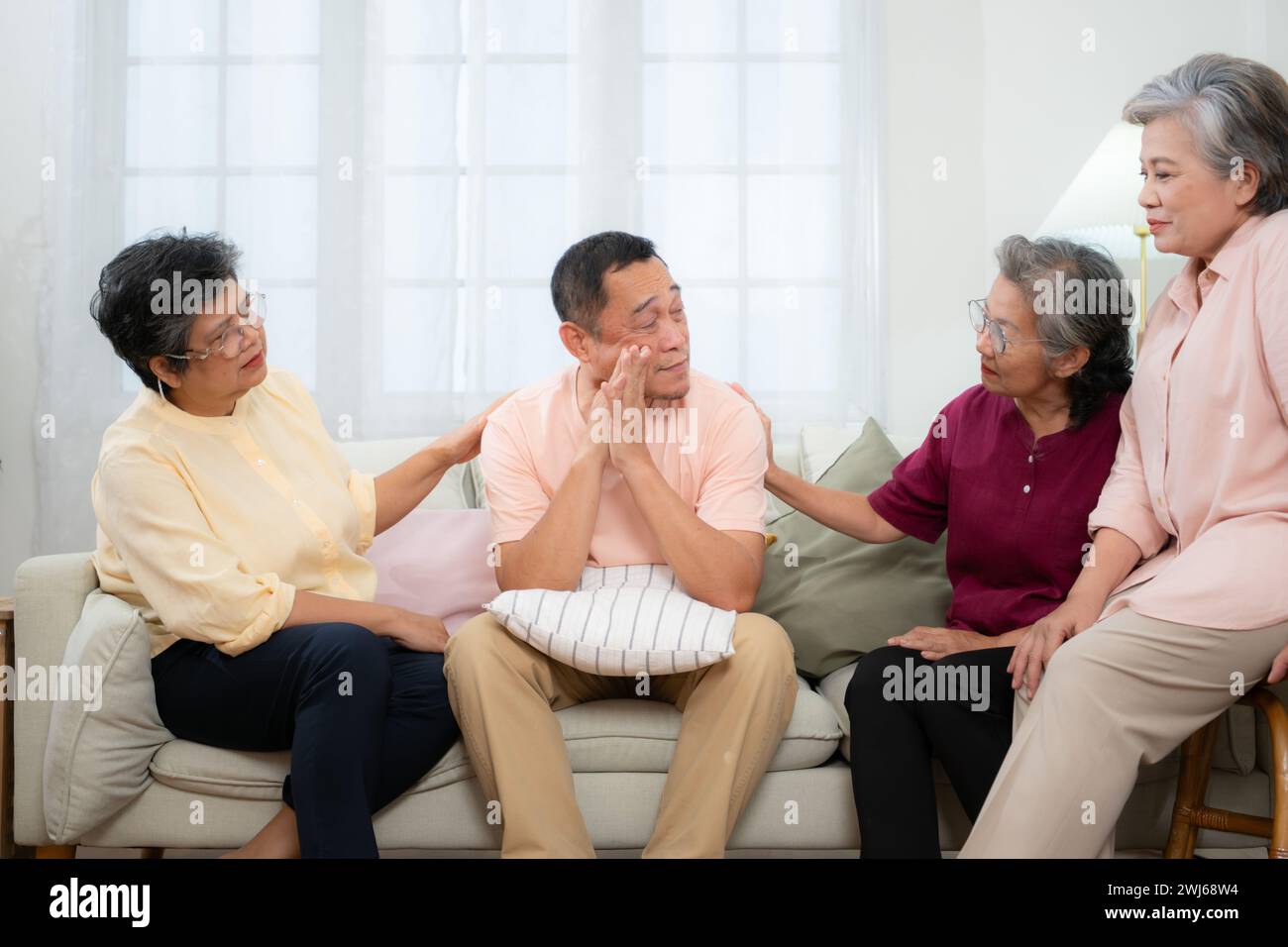 Senior asiatischer Mann, der an einer schweren Krankheit leidet, sitzt auf dem Sofa mit Freunden, die zu Besuch kommen, und ermutigt die Stockfoto