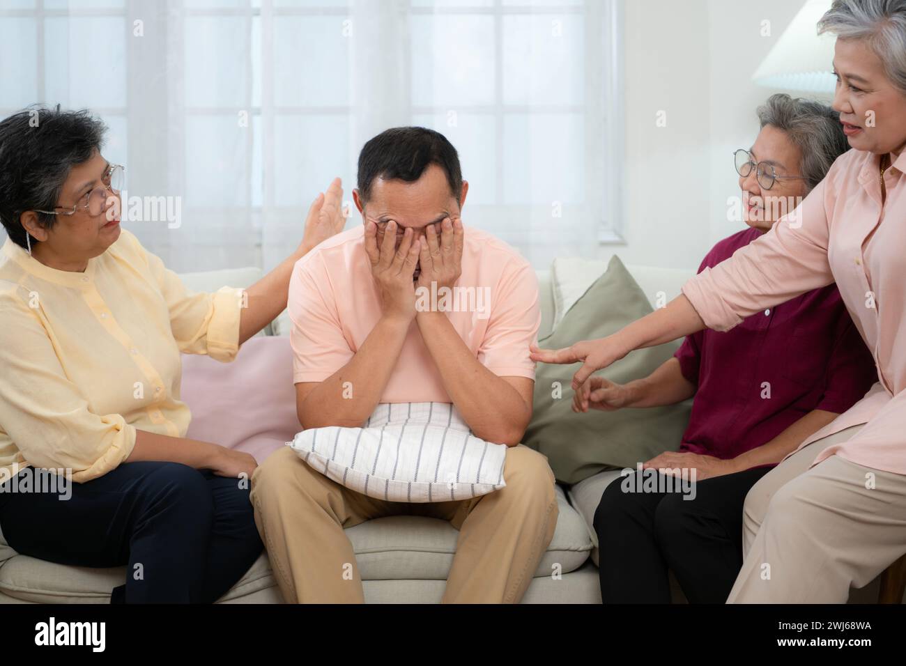 Senior asiatischer Mann, der an einer schweren Krankheit leidet, sitzt auf dem Sofa mit Freunden, die zu Besuch kommen, und ermutigt die Stockfoto