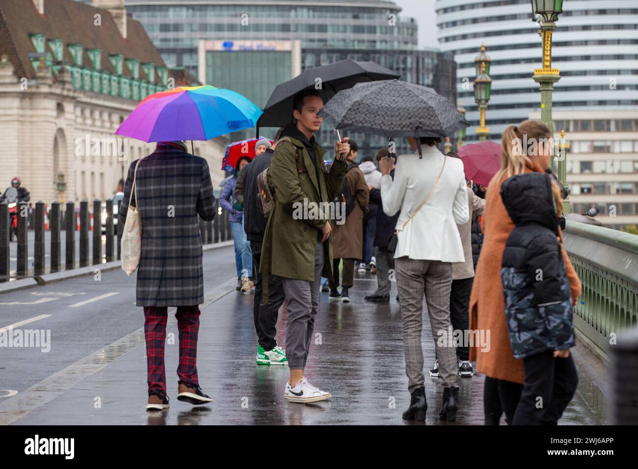 London, UK, 13. Februar 2024 Touristenwarteschlange im Regen mit Regenschirmen, um Fotos von der ikonischen Red Phone Box in London zu machen und die Sehenswürdigkeiten in London trotz Regen zu genießen Credit: Richard Lincoln/Alamy Live News Stockfoto